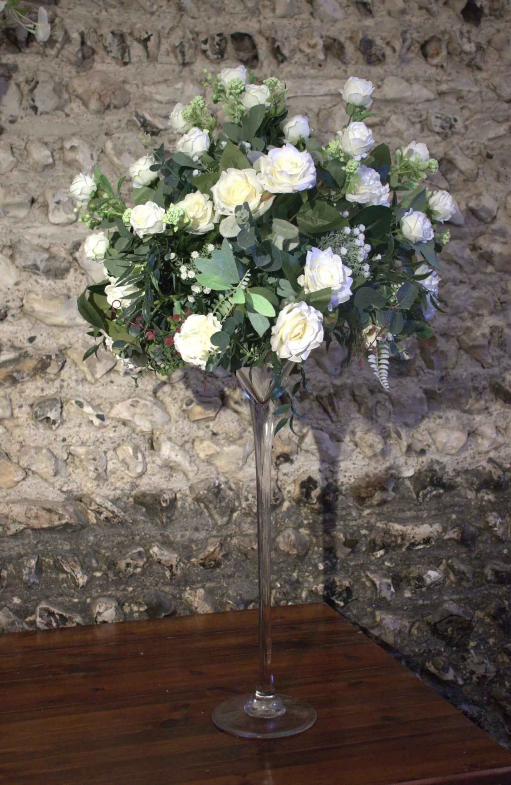 Martini Glass Centrepiece with Faux Flower featuring white faux roses and greenery in a tall clear vase, available to hire for your wedding or event.