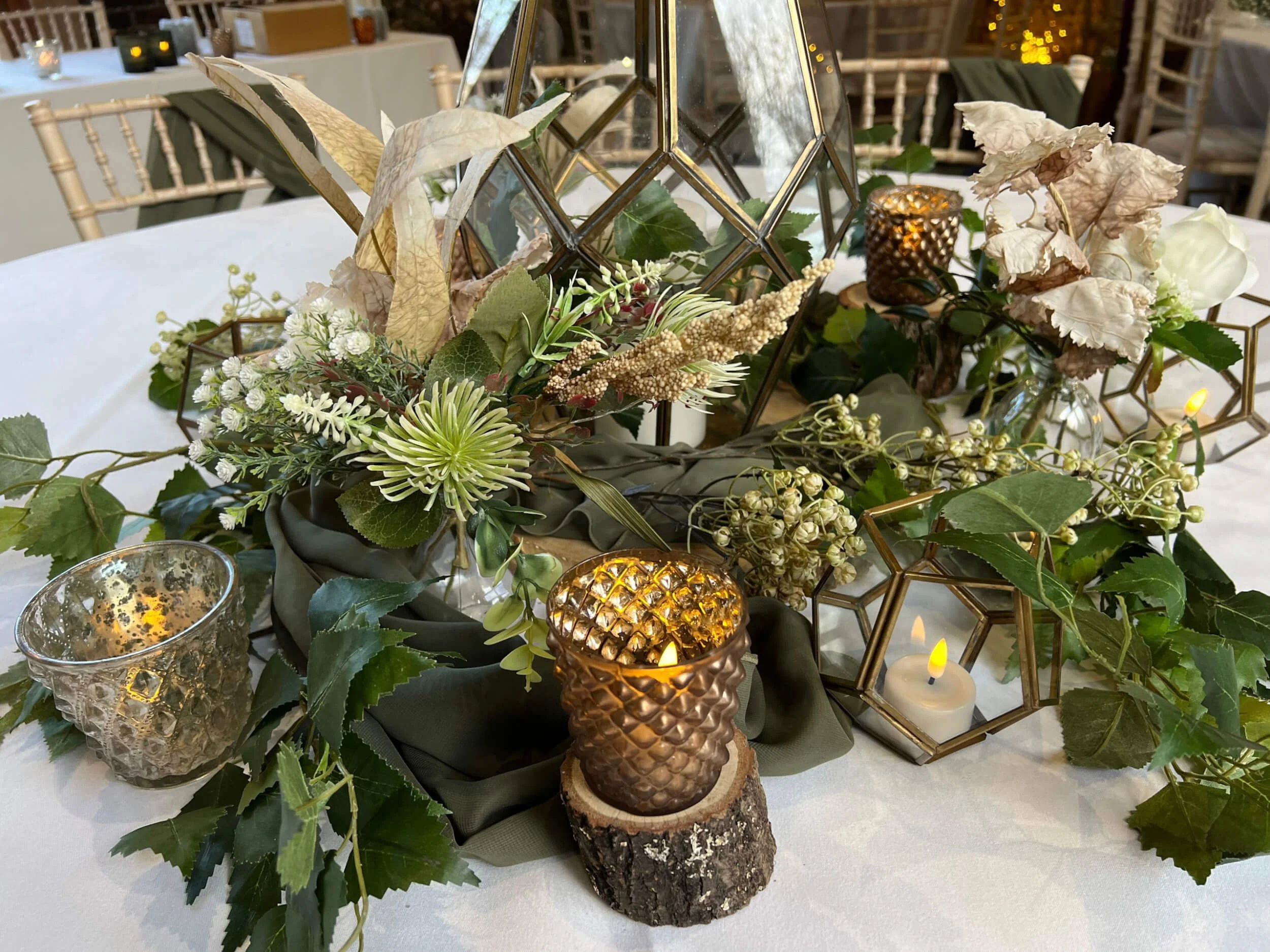 Mini Raised Logs used as rustic bases for candle holders, available to hire for your wedding or event with floral and greenery accents.