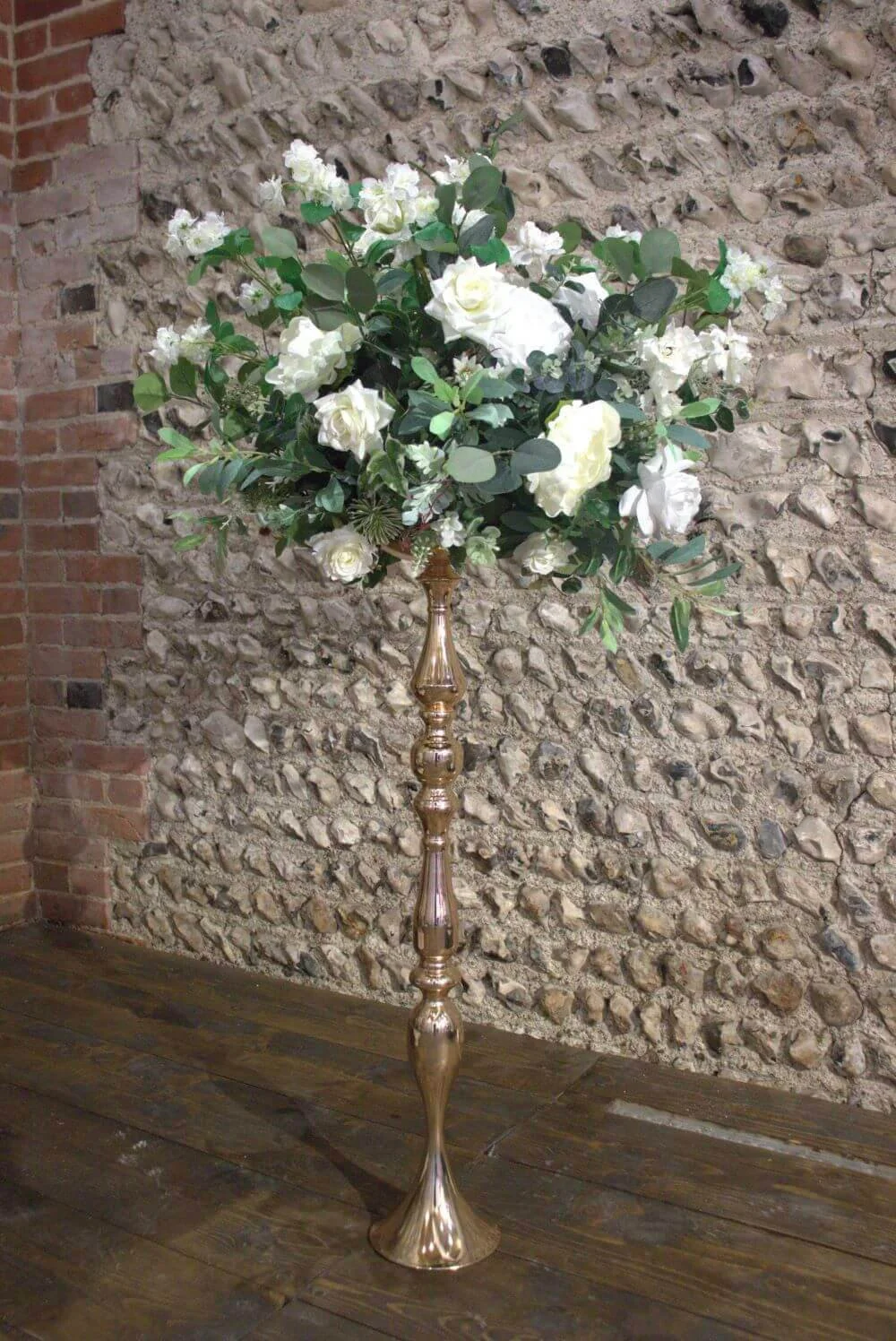 Ornate Gold Floral Stand with white flowers and greenery, available to hire for your wedding or event.