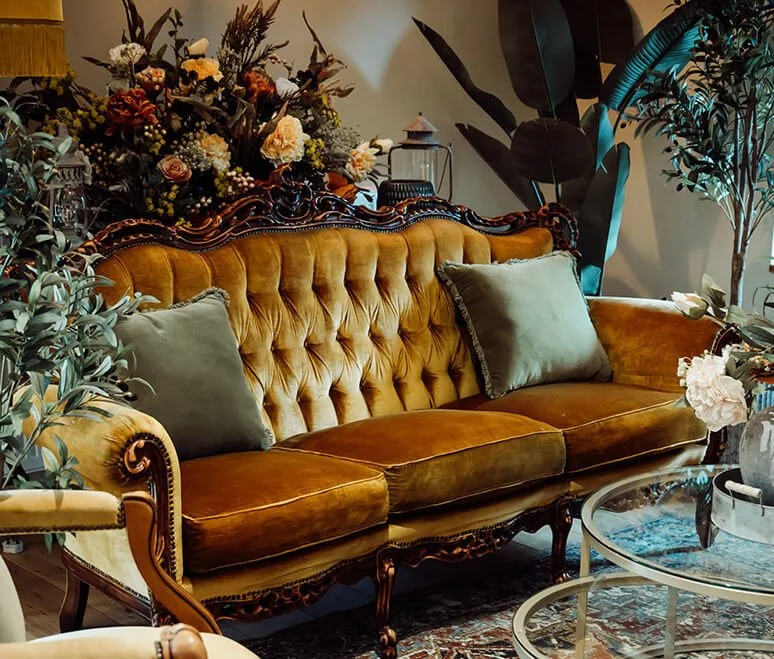 Green Velvet Cushion - 43cm placed on a vintage mustard yellow sofa, available to hire for your wedding or event.