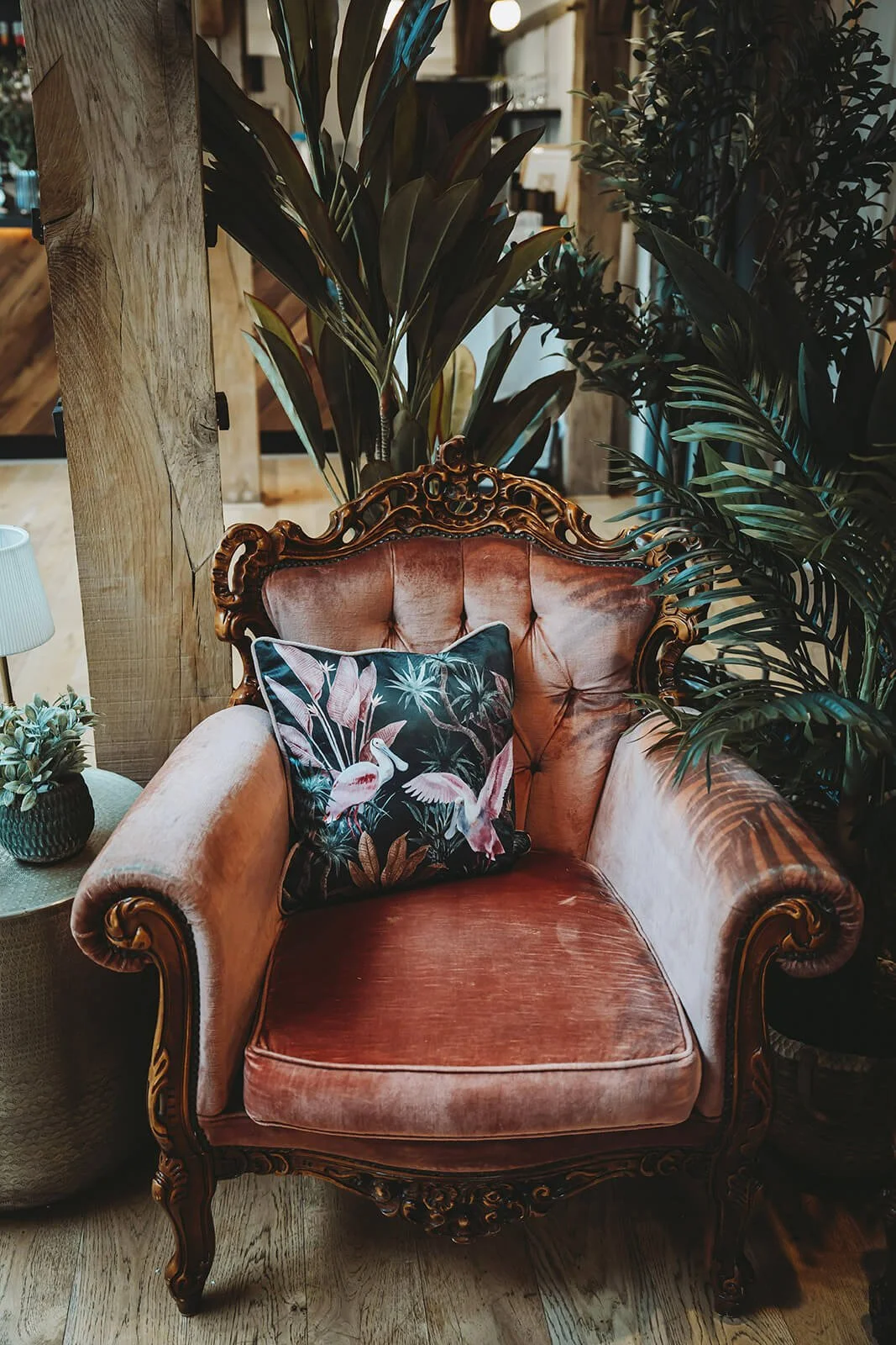 Tropical Pink Cushion - 43cm with flamingo and foliage design on dark background, placed on pink velvet armchair, available to hire for your wedding or event.