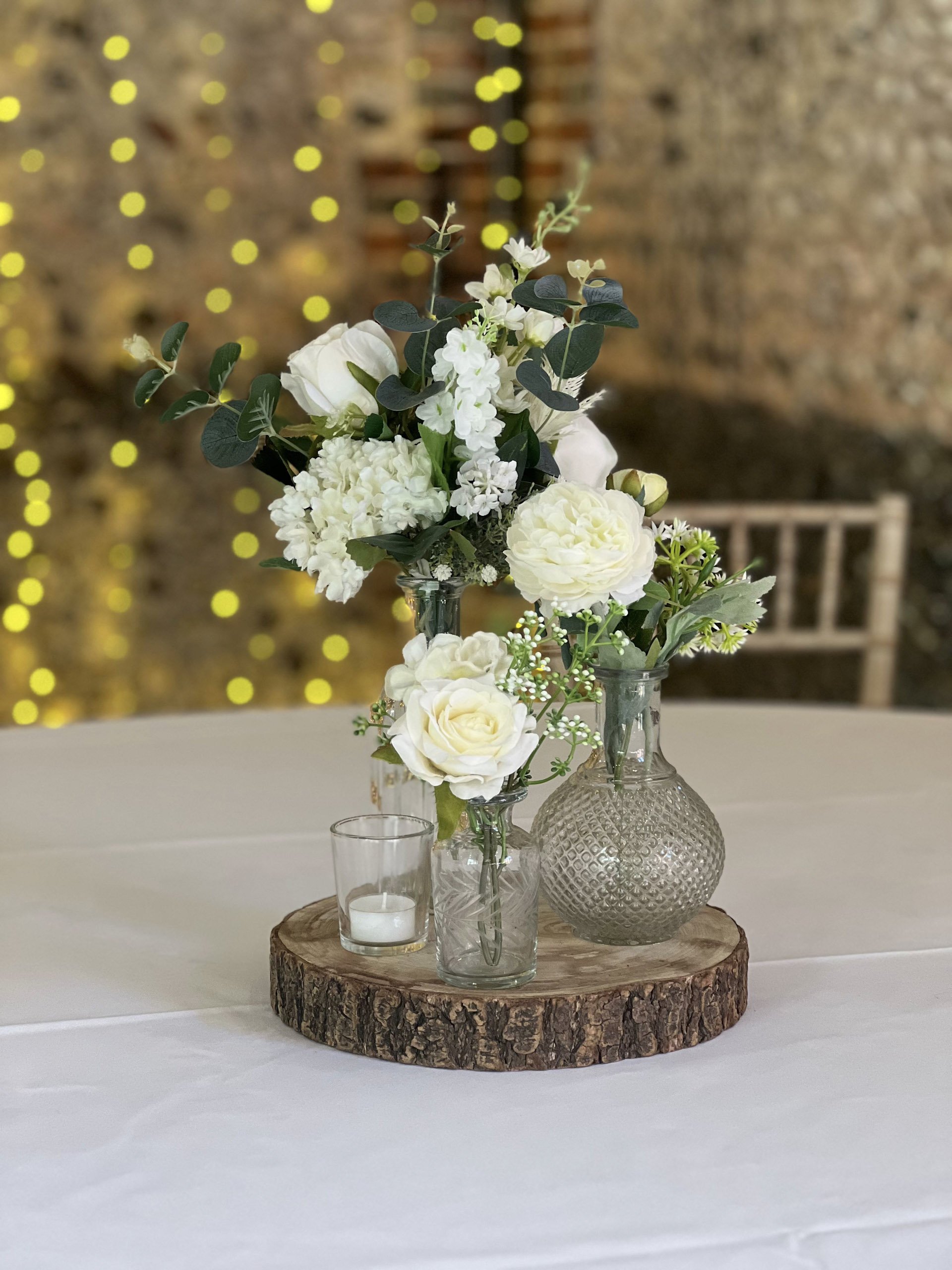 Log Slices used as a natural wood base with glass vases and white flowers, available to hire for your wedding or event.