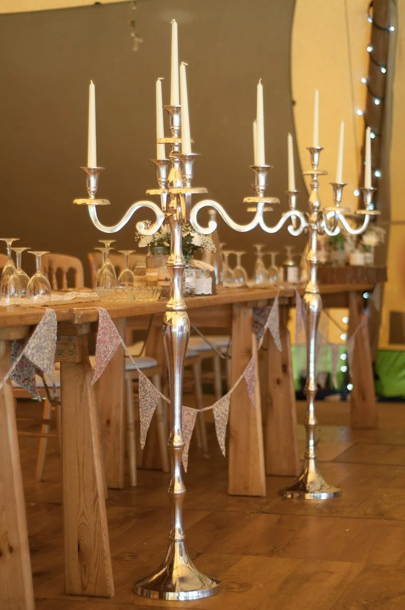 Candelabra Floorstanding Silver - 120cm with white taper candles, available to hire for your wedding or event, shown beside a decorated wooden table.
