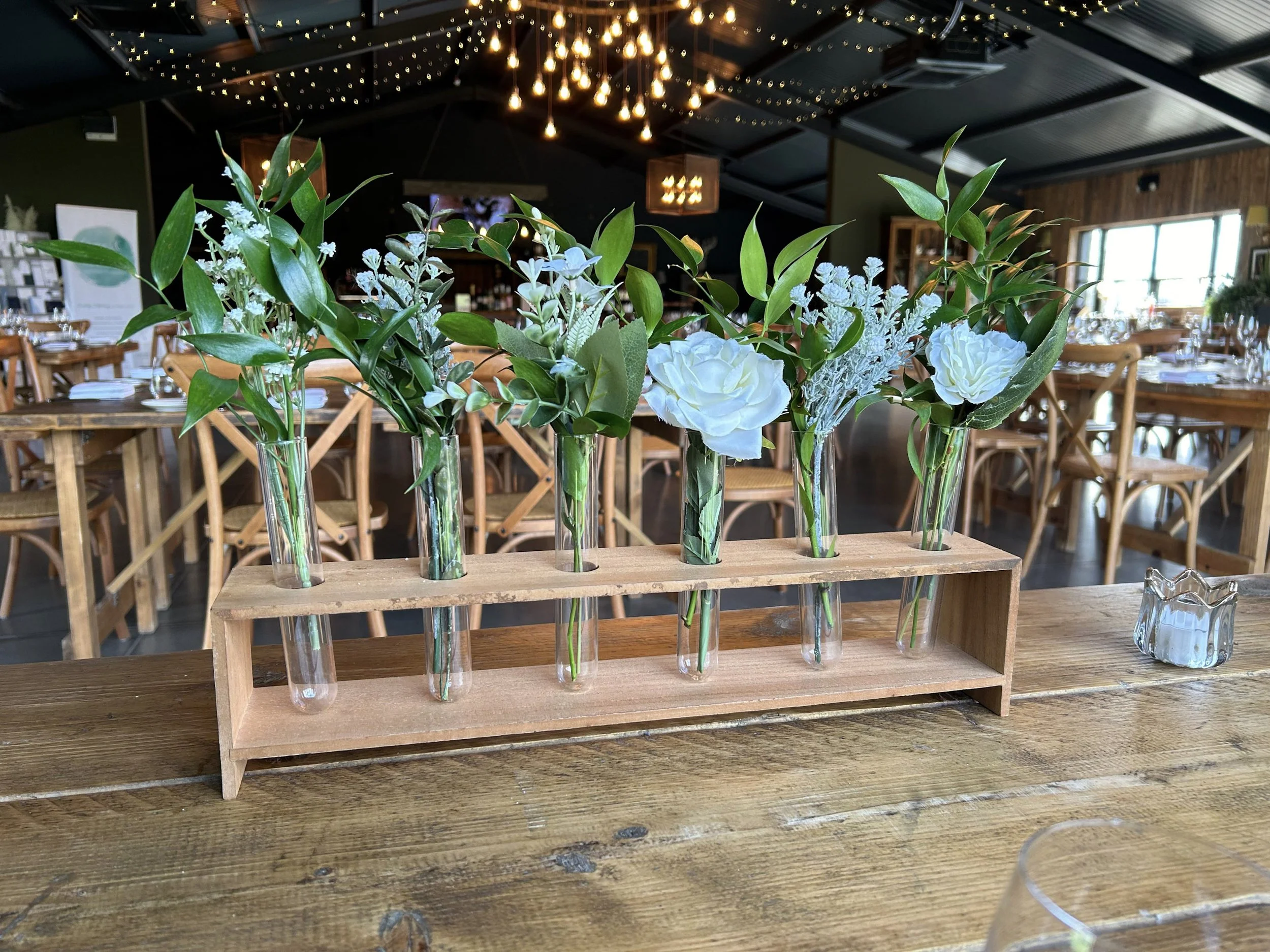 Rustic Stem Centrepiece - 6 containers 19cm H x 45cm xL x 8cm W with green foliage and white flowers in glass tubes on wooden holder, available to hire for your wedding or event.