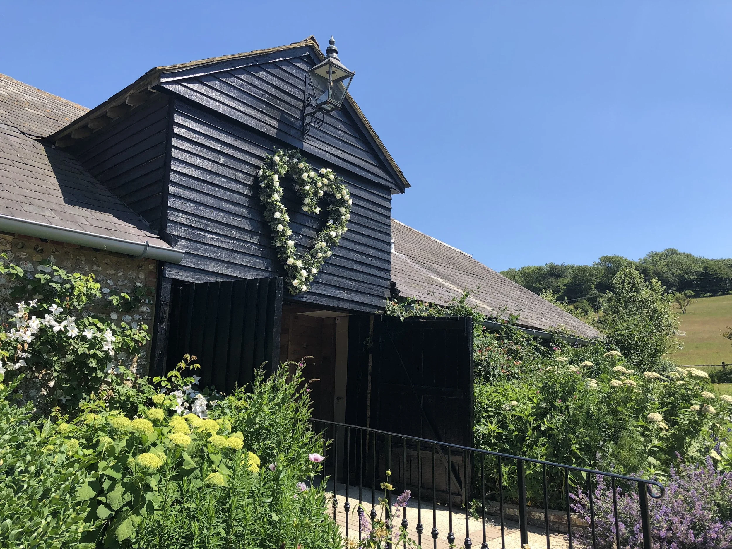Giant Heart floral wreath with white flowers and greenery on a black barn wall, available to hire for your wedding or event.