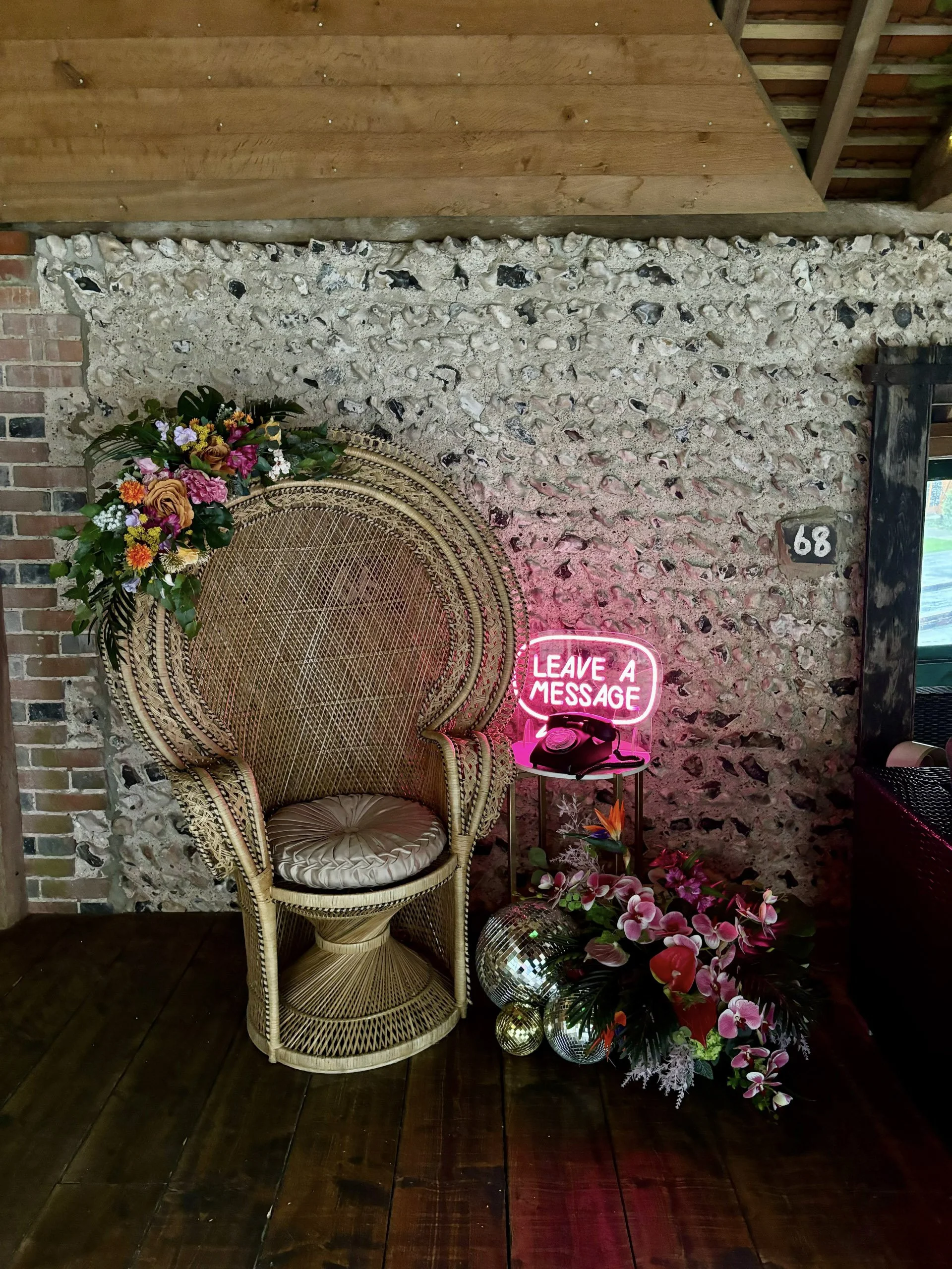Peacock Wicker Chair with floral decoration, available to hire for your wedding or event, shown in a rustic indoor setting with stone wall and wooden floor.