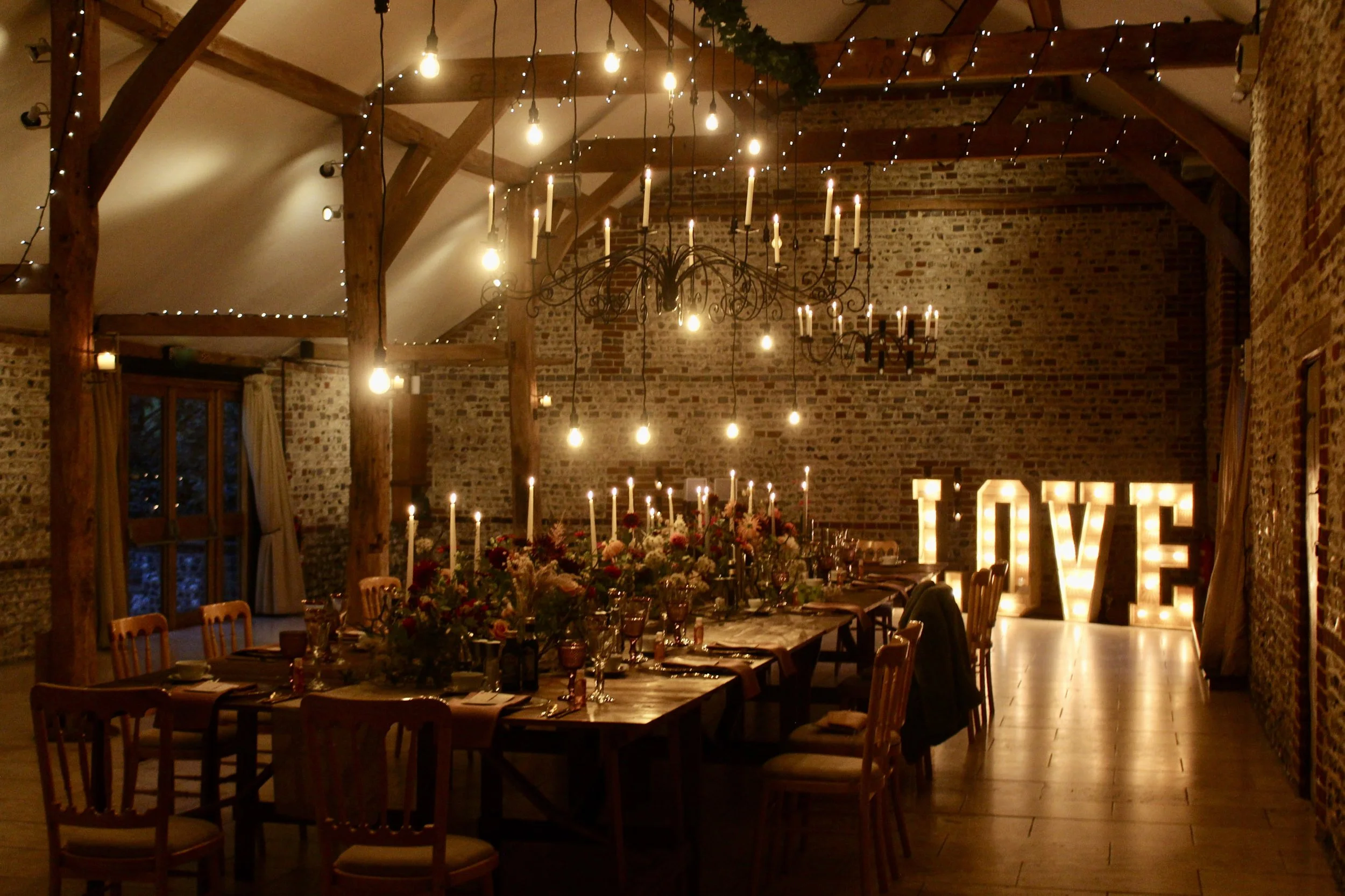 Giant Light Up Letters Rustic Love illuminated in a rustic venue with wooden beams and brick walls, available to hire for your wedding or event.