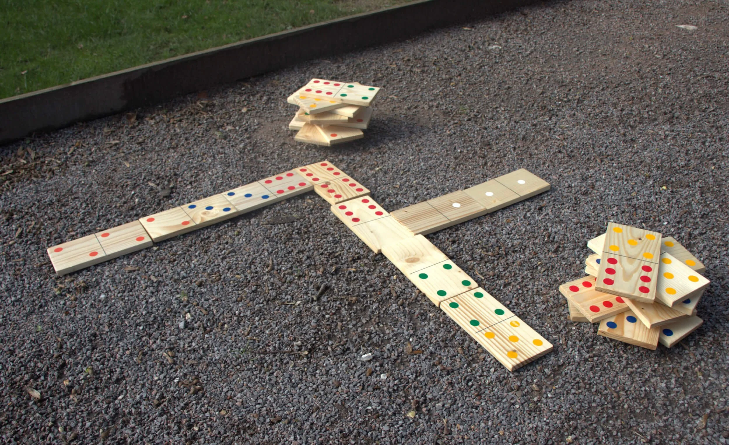 Giant Dominoes with coloured dots on wooden pieces, available to hire for your wedding or event, set outdoors on gravel.
