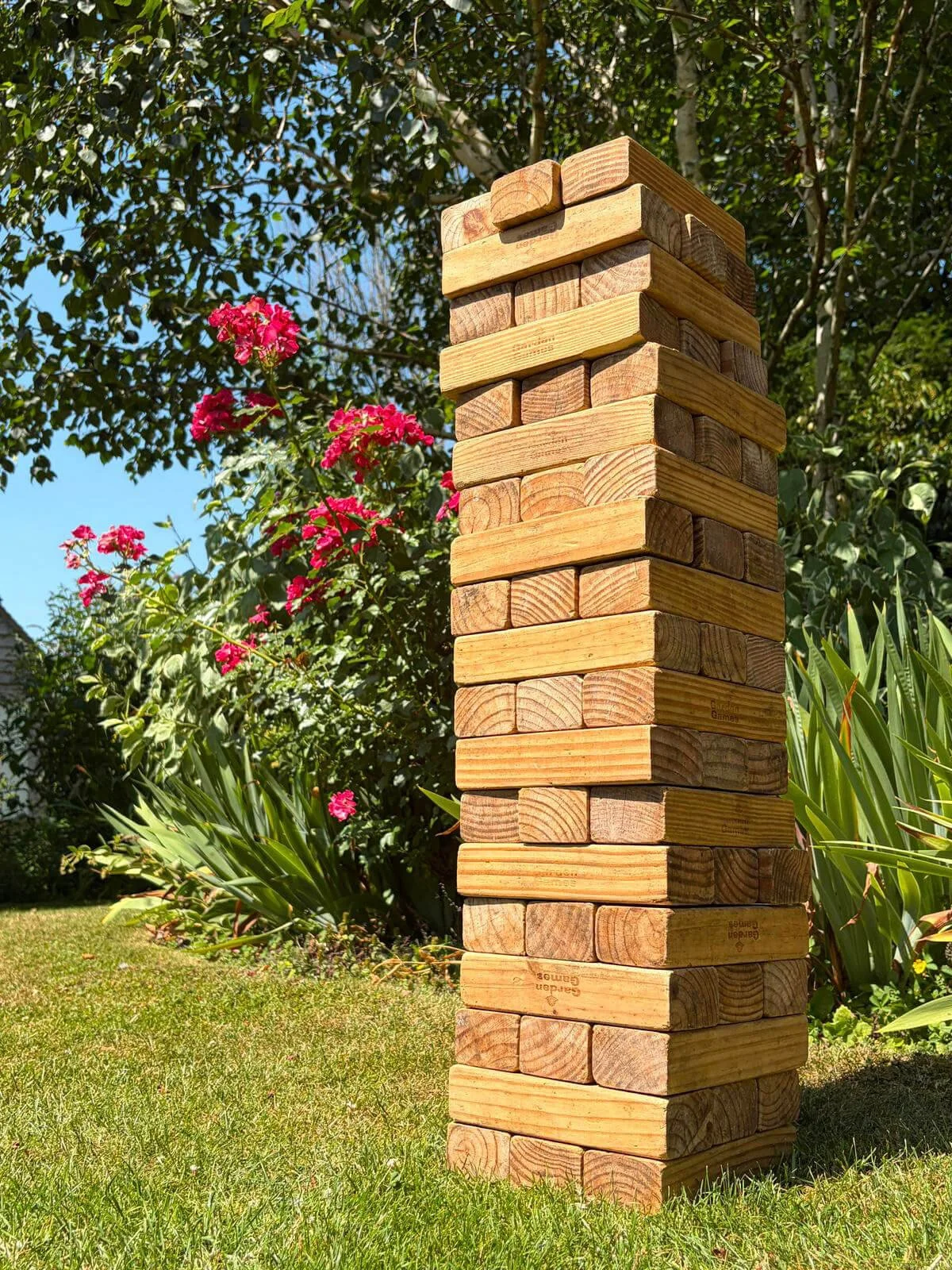 Giant Jenga made of large wooden blocks stacked outdoors on grass, available to hire for your wedding or event.