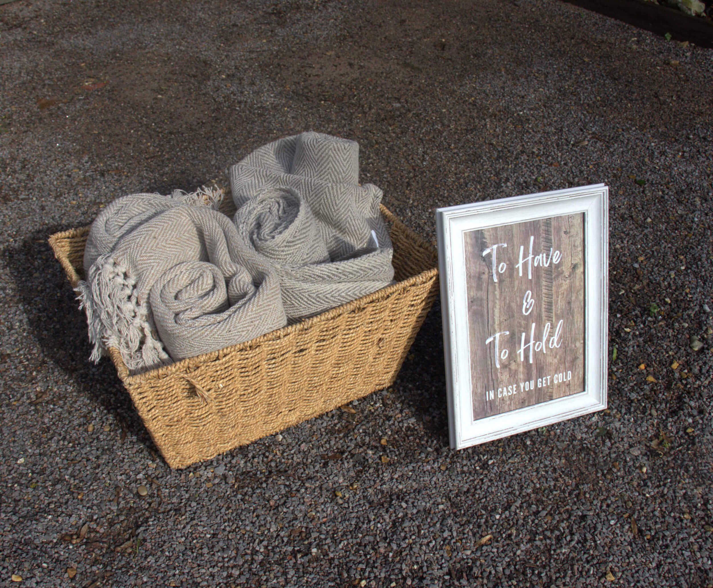 Basket of Cuddle Blankets - Standard with rolled grey blankets in a woven basket, available to hire for your wedding or event.