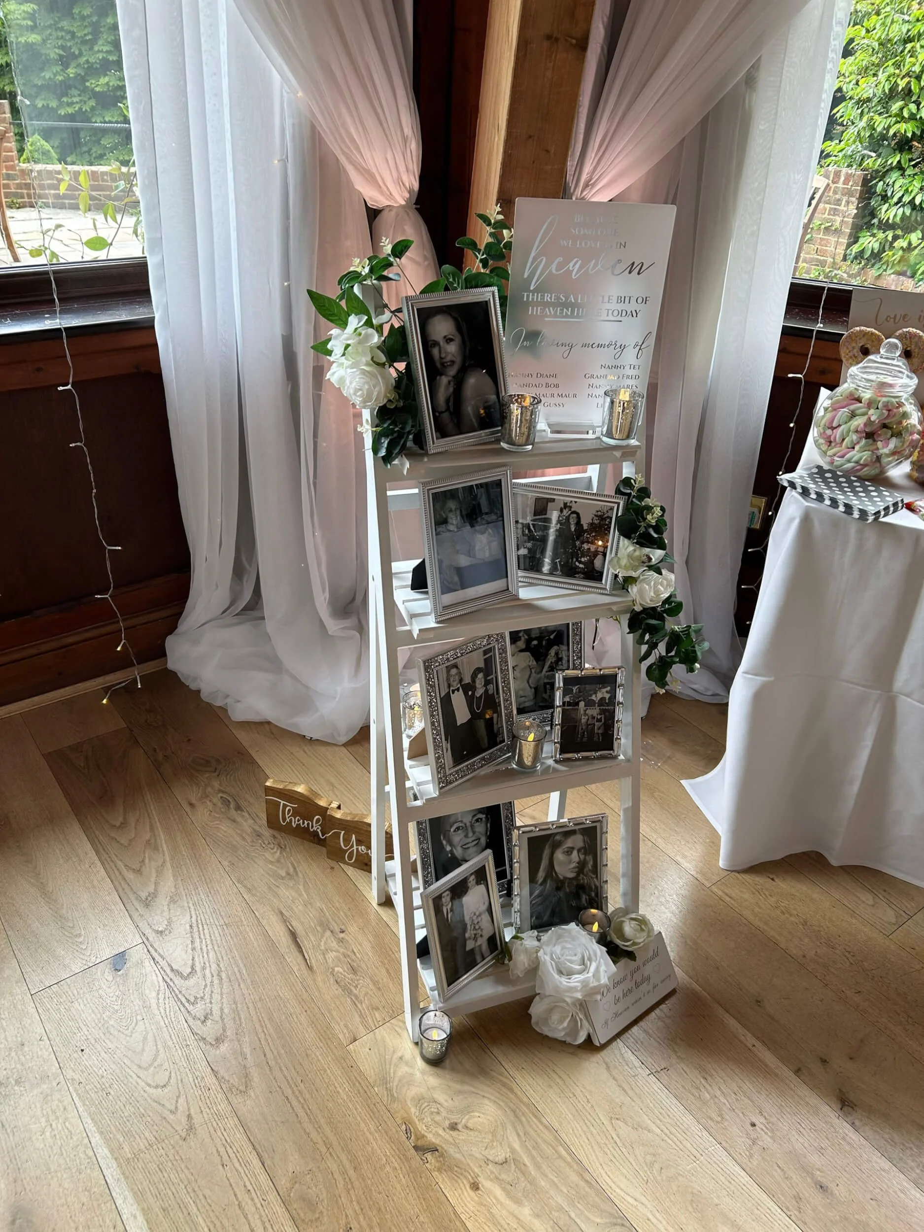 In Memory of Set Up with framed photos, faux white flowers, candles, and a memorial sign, available to hire for your wedding or event.