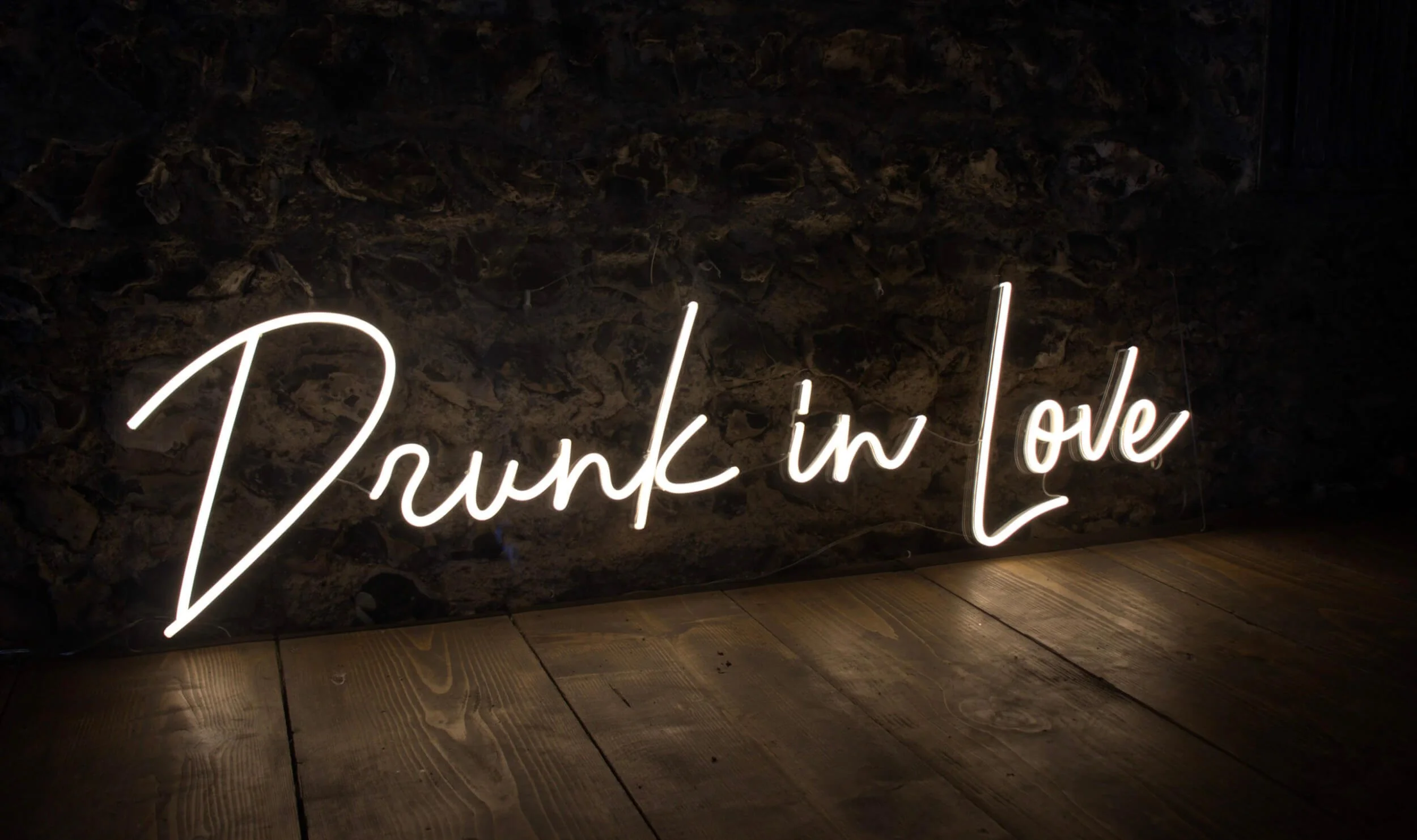 Drunk in Love Neon Sign in white neon light against a dark stone wall, available to hire for your wedding or event.