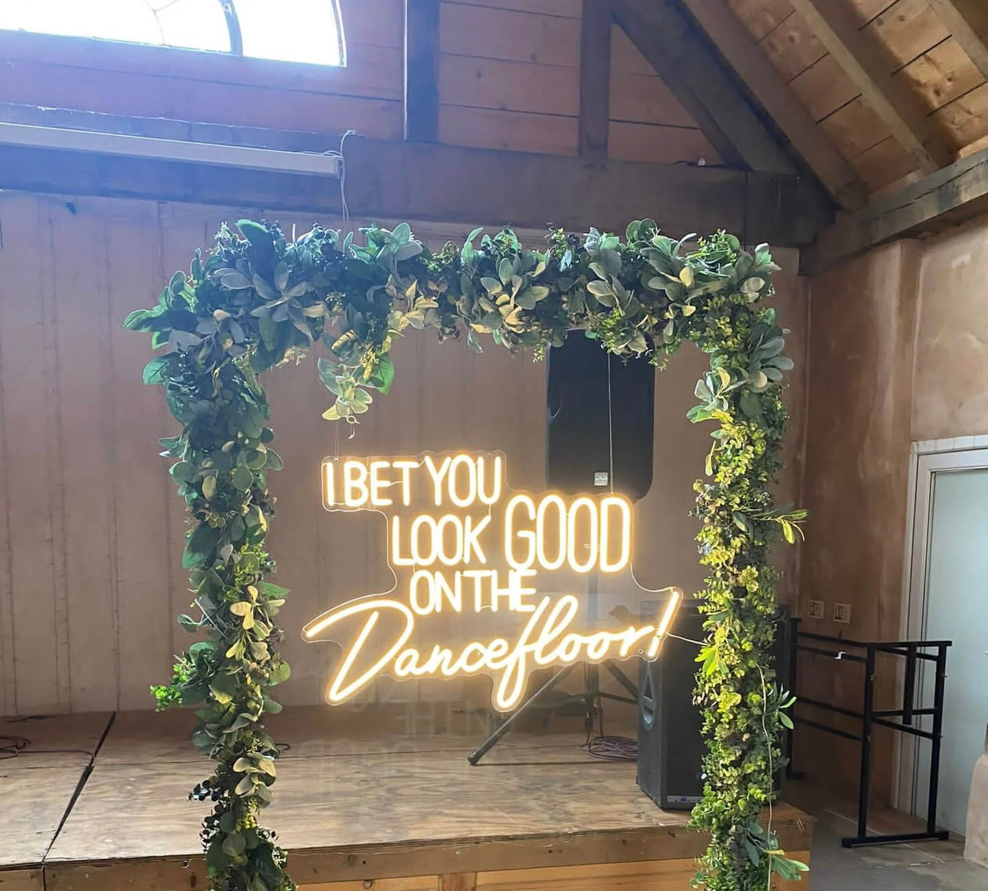 I Bet That You Look Good on the Dancefloor Neon Sign in yellow neon framed by green foliage arch, available to hire for your wedding or event.