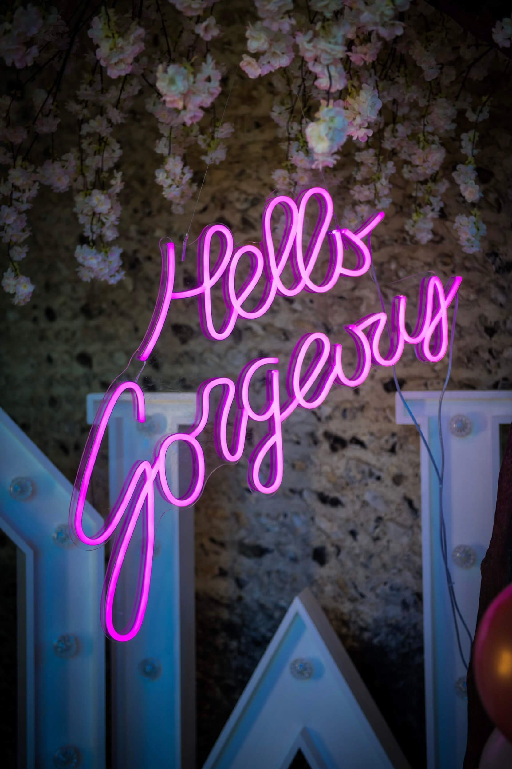 Hello Gorgeous Neon Sign in bright pink neon, hanging with white flowers above, available to hire for your wedding or event.