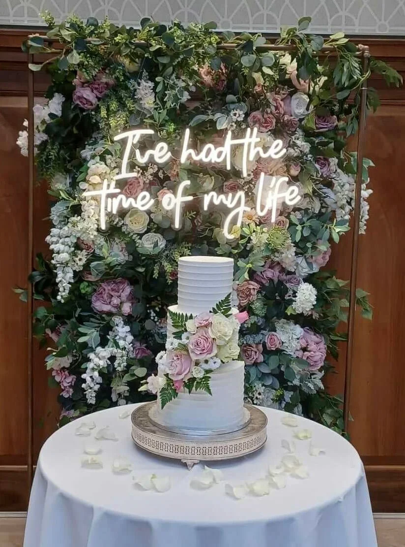 I've had the time of my life neon sign in white on a floral backdrop with pink and white flowers, available to hire for your wedding or event.