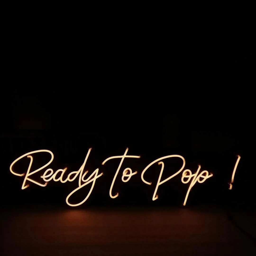 Ready to Pop! Neon Sign glowing in warm white light, available to hire for your wedding or event.