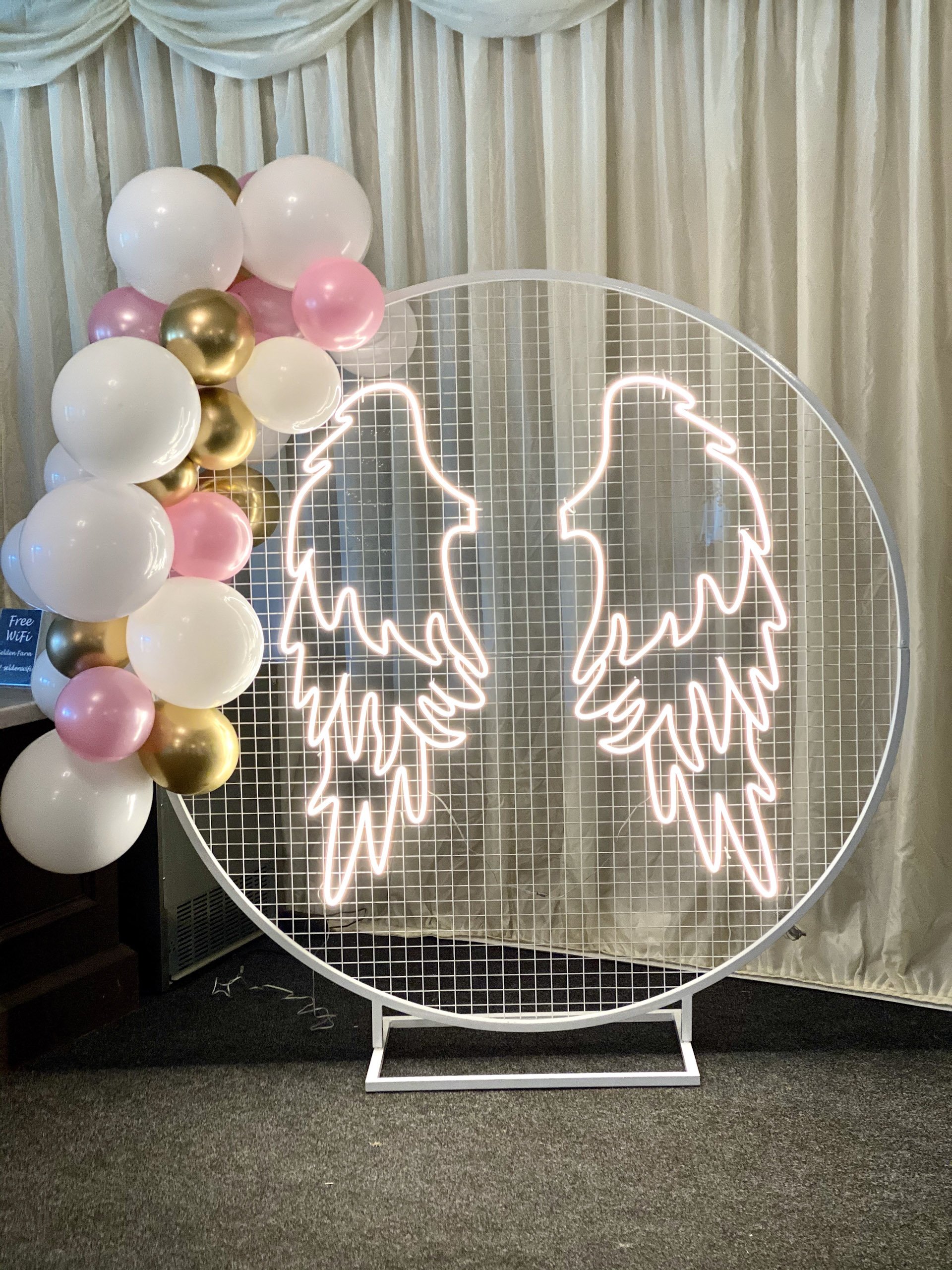Mesh Circle Frame - White with neon angel wings and balloon decoration, available to hire for your wedding or event.