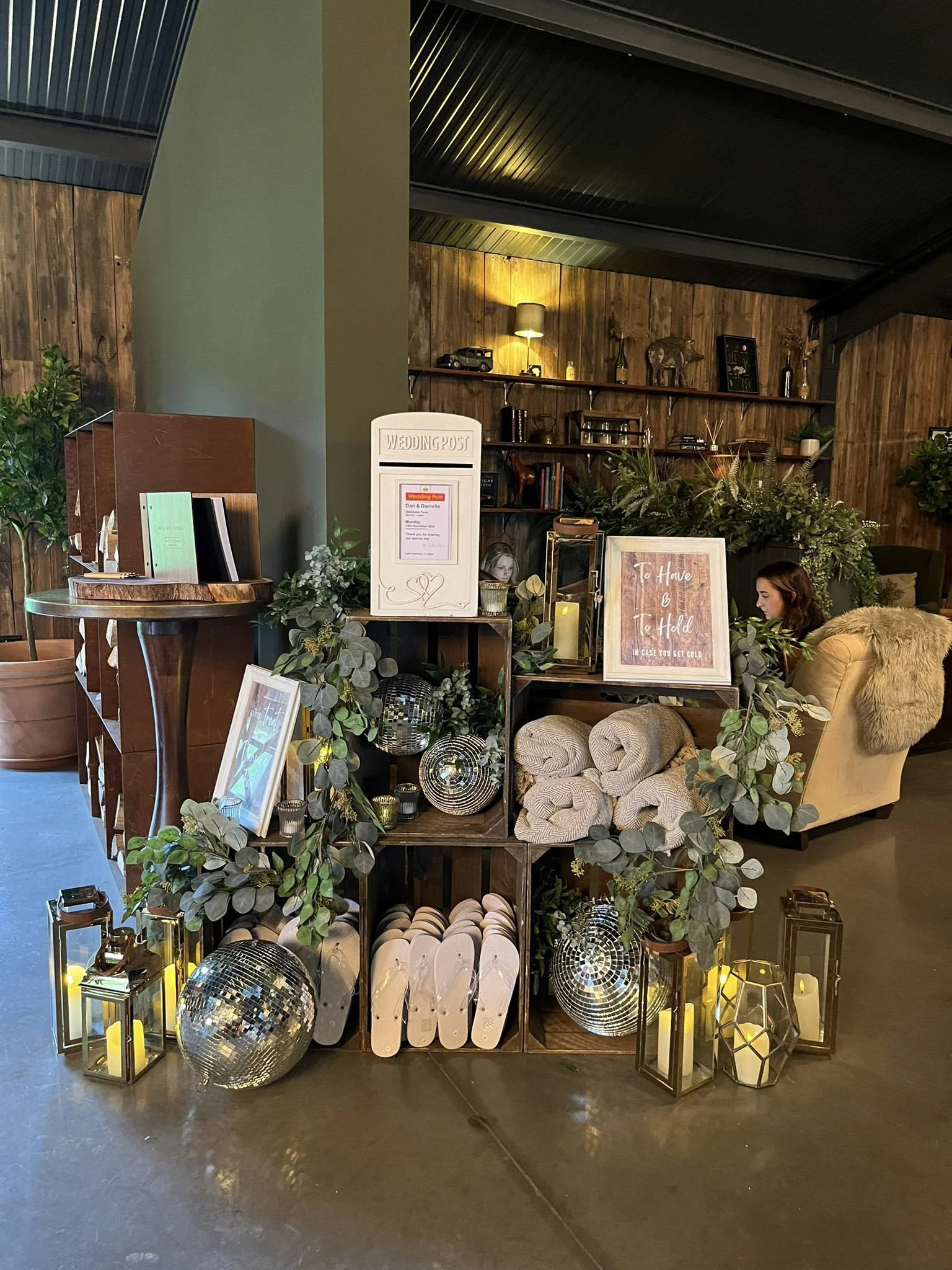 Rustic Guest Stack - Sweets, Blankets, Guest Book, Flip Flops arranged with greenery, disco balls, lanterns and a wedding post box, available to hire for your wedding or event.