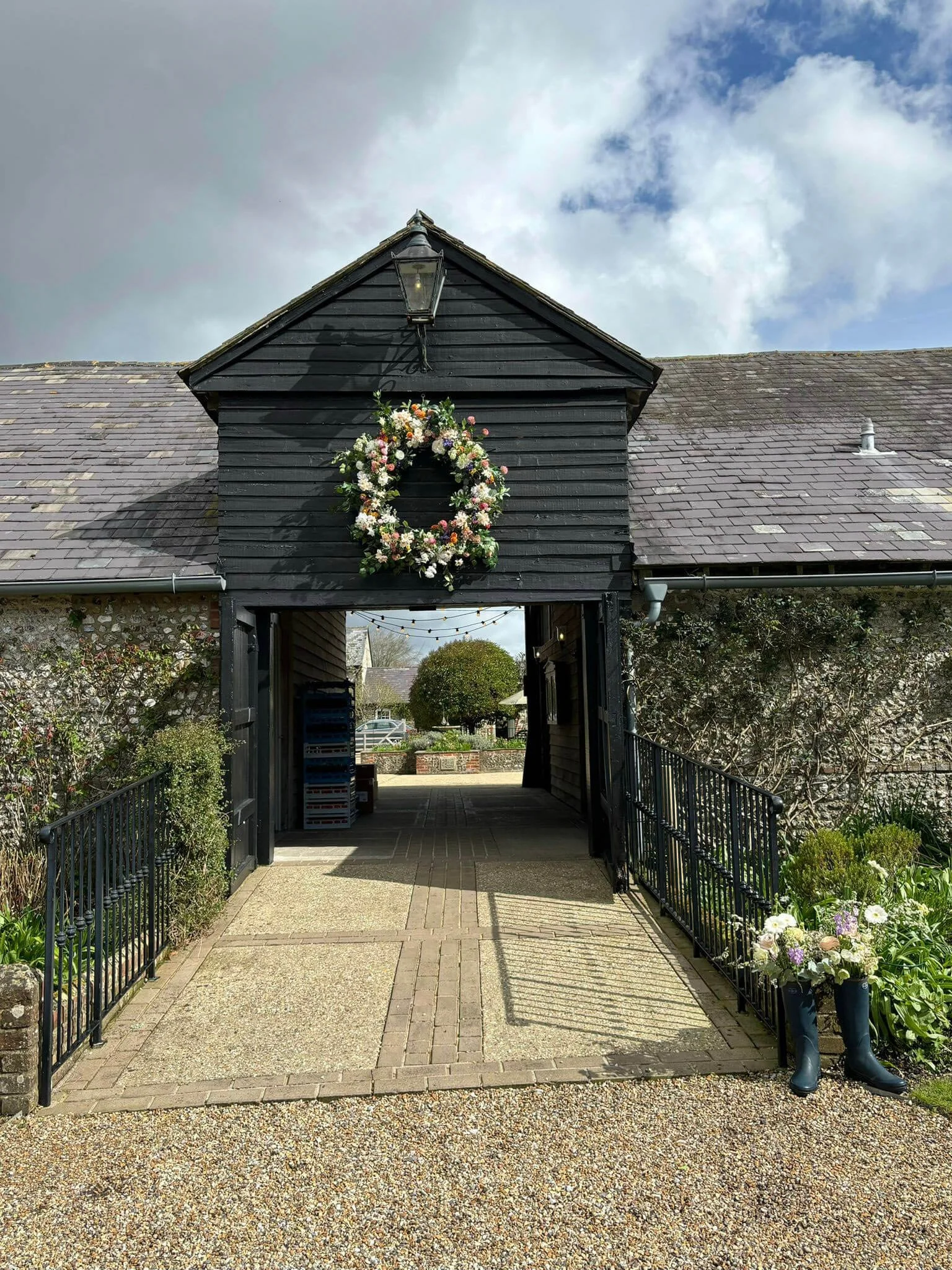 Giant Round Wreath with pastel and white flowers and greenery, hanging on a black barn entrance, available to hire for your wedding or event.