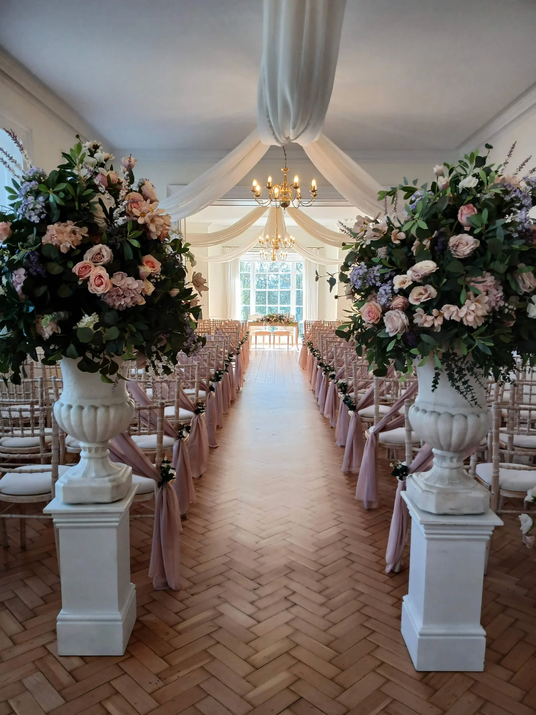 Ornate Urn with Faux foilage and flowers - Bespoke colours, white urns with pink and purple faux flowers on pedestals, available to hire for your wedding or event.