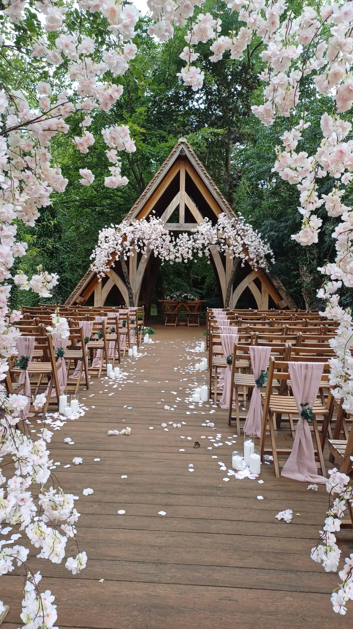 Faux Petals down the aisle with soft pink fabric on chairs and white candles lining the wooden aisle, available to hire for your wedding or event.