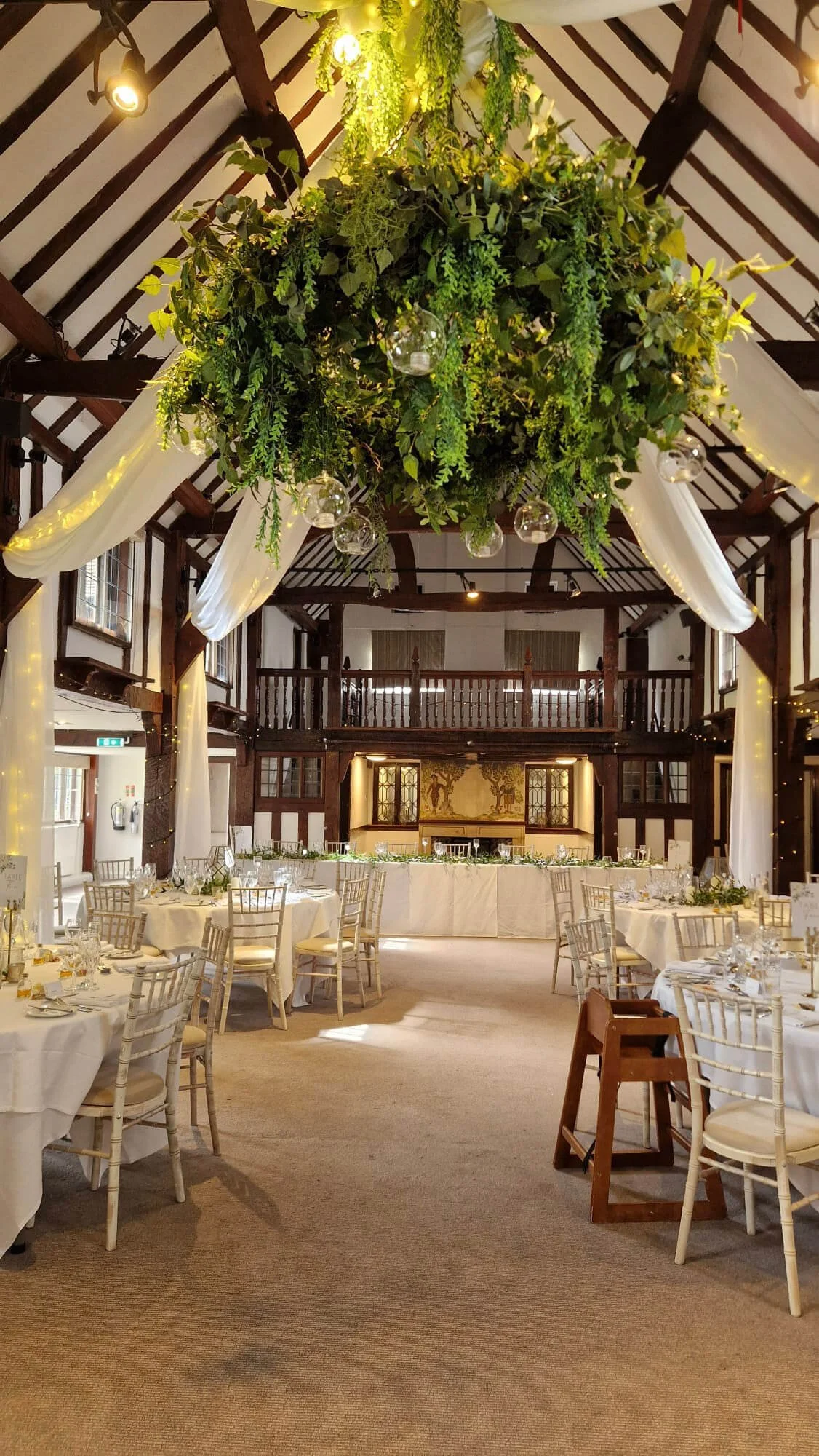Faux Foliage Chandelier with hanging glass globes, available to hire for your wedding or event in a decorated venue with white drapes and set tables.