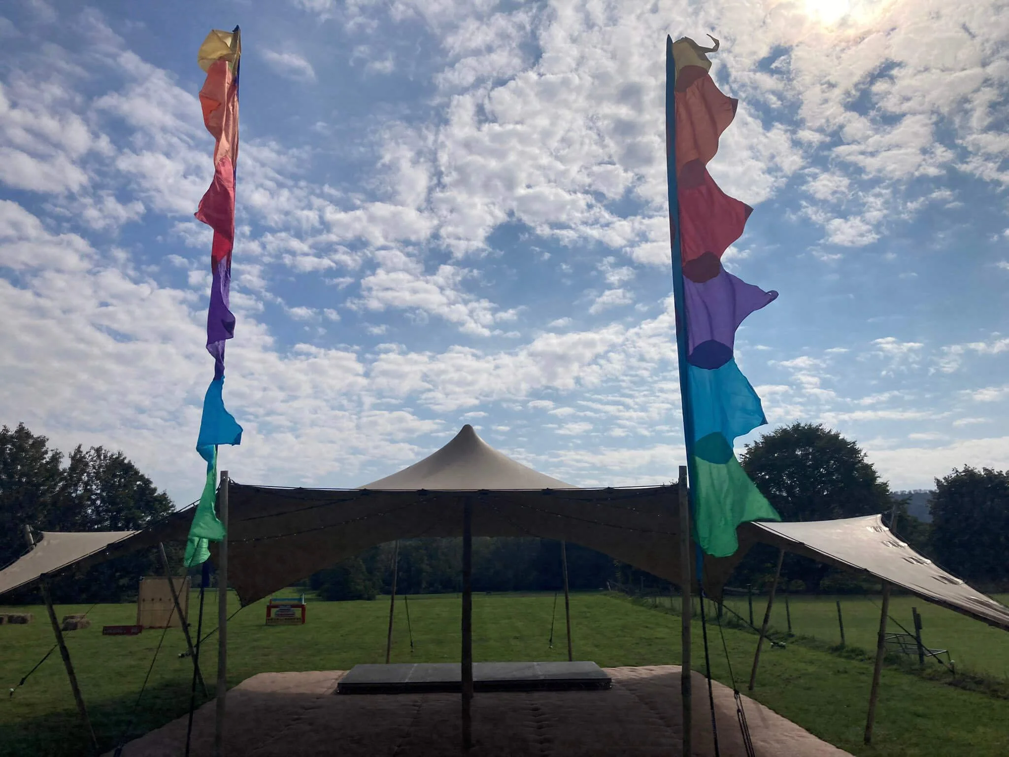 Festival Flag with multicoloured sections available to hire for your wedding or event, shown fluttering above an outdoor tent in a field.