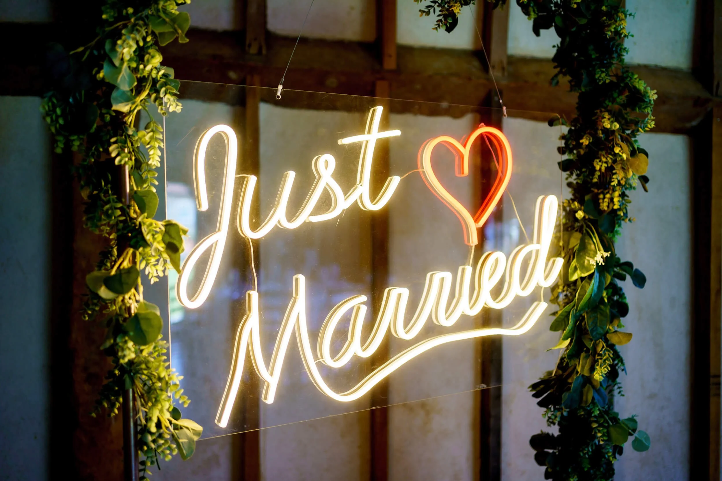 Just Married Neon Sign with red heart and white lettering, framed by green foliage garlands, available to hire for your wedding or event.