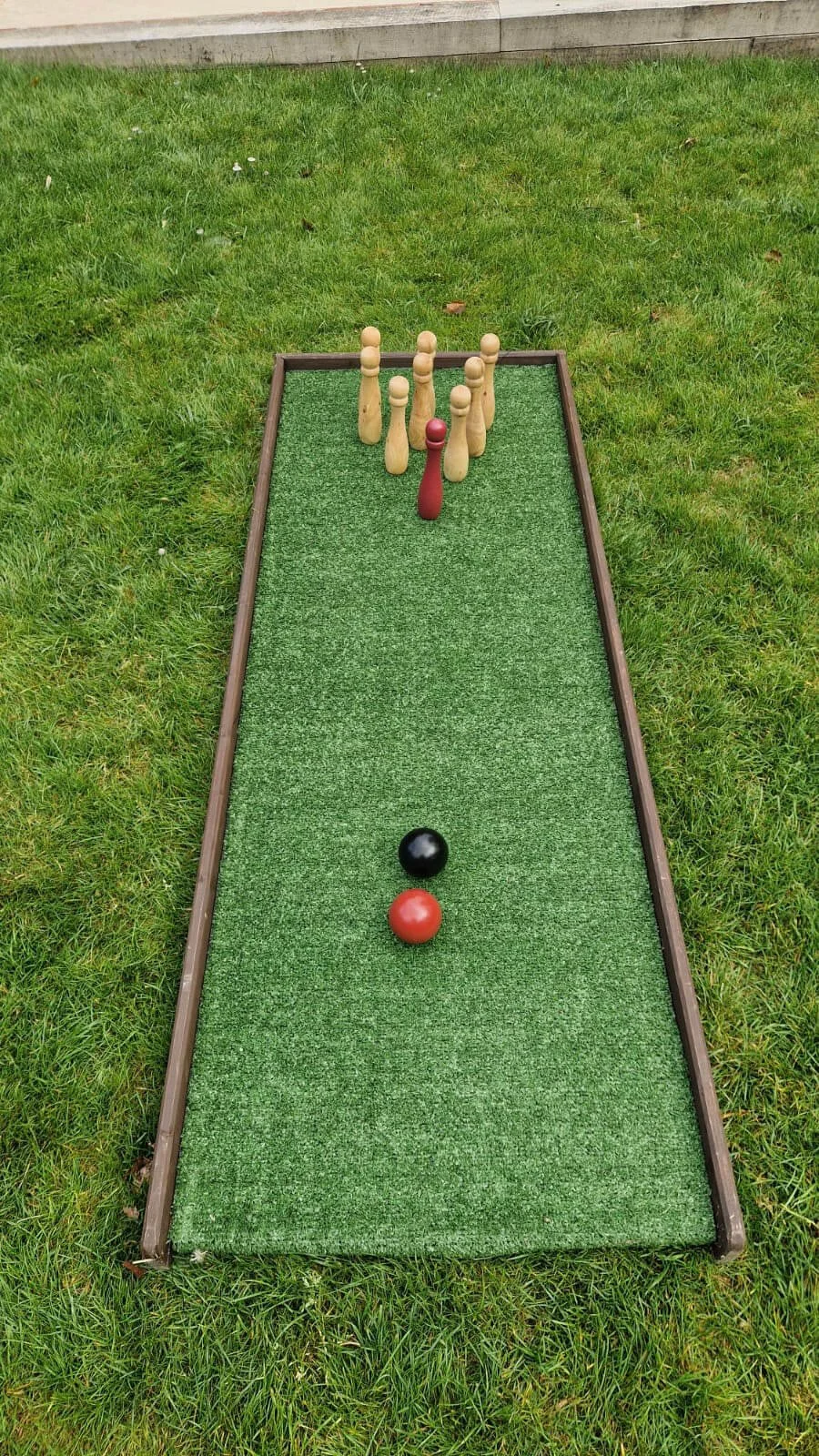 Skittles & Skittle Board with wooden skittles and two balls on a green turf board, available to hire for your wedding or event.