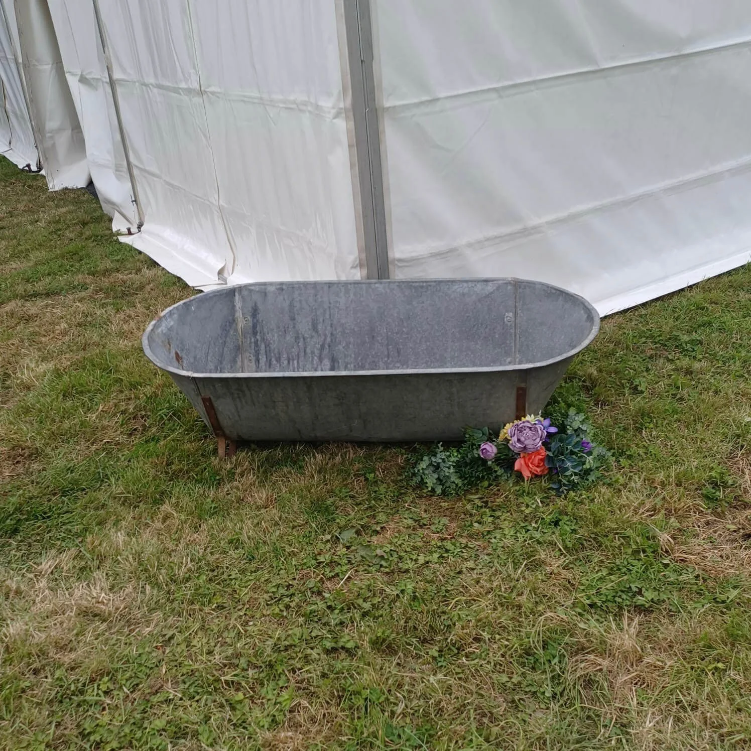 Vintage Tin Bath available to hire for your wedding or event, shown outdoors on grass next to a white marquee with floral decoration.
