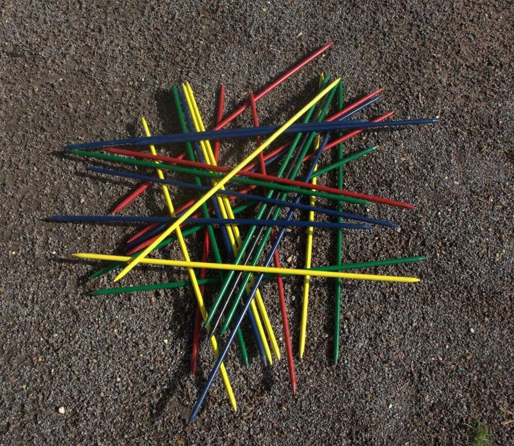 Giant Pick Up Sticks in red, yellow, green, and blue scattered on gravel, available to hire for your wedding or event.