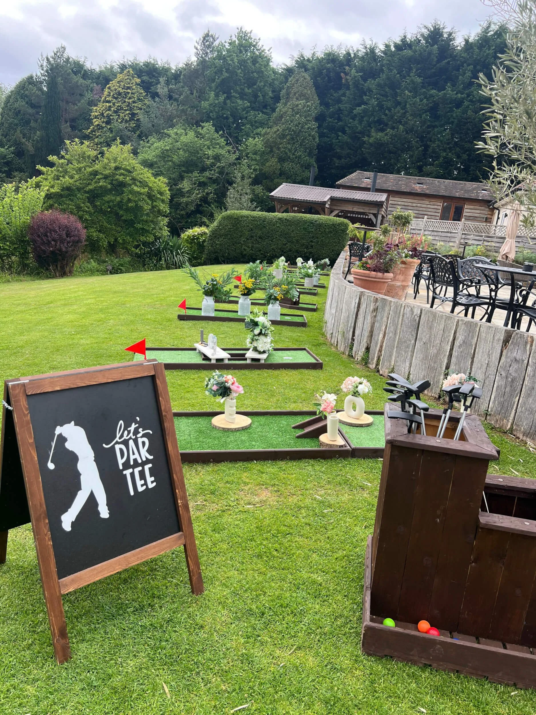 Mini Golf - 9 Hole Set with floral decorations and red flags on green lawn, available to hire for your wedding or event.