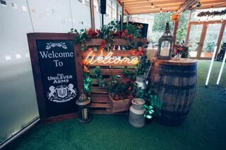 Welcome Neon Sign in orange mounted on wooden crate with plants and lanterns, available to hire for your wedding or event.