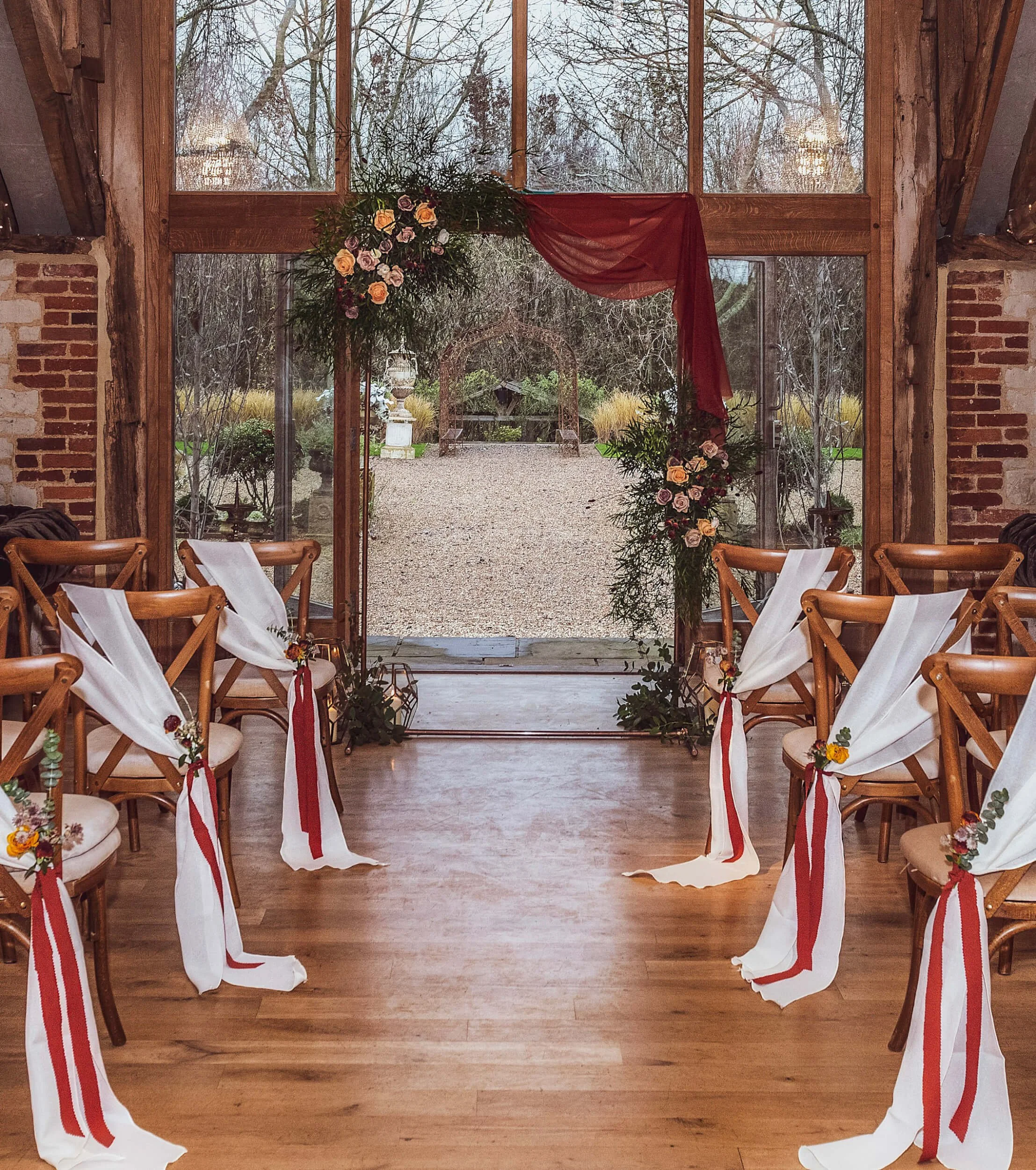 Copper Arch decorated with greenery, peach and purple flowers, and burgundy fabric, available to hire for your wedding or event.
