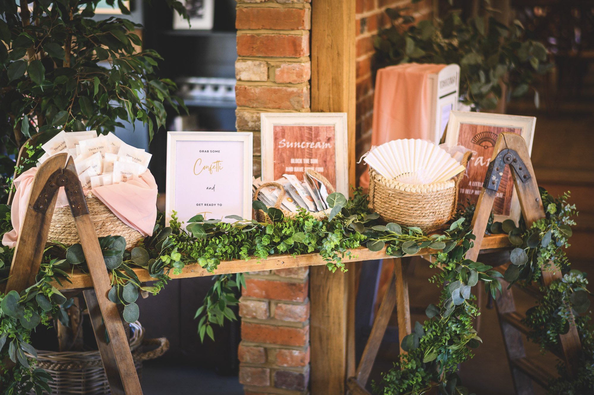 Rustic Ladder Table decorated with greenery, wicker baskets, fans, and framed signs, available to hire for your wedding or event.