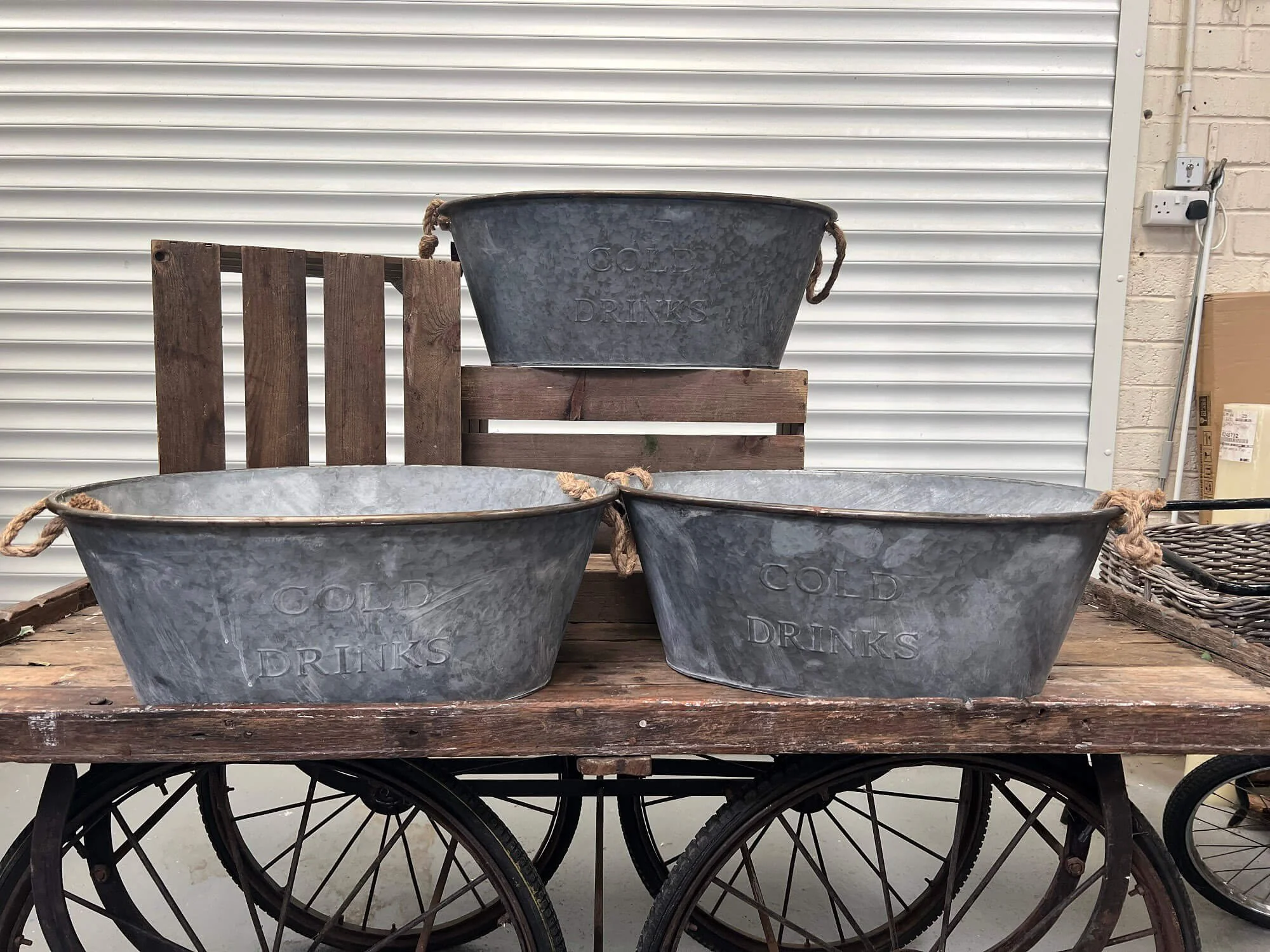 Galvanised Drinks Bucket with rope handles, displayed on a wooden cart and crates, available to hire for your wedding or event.