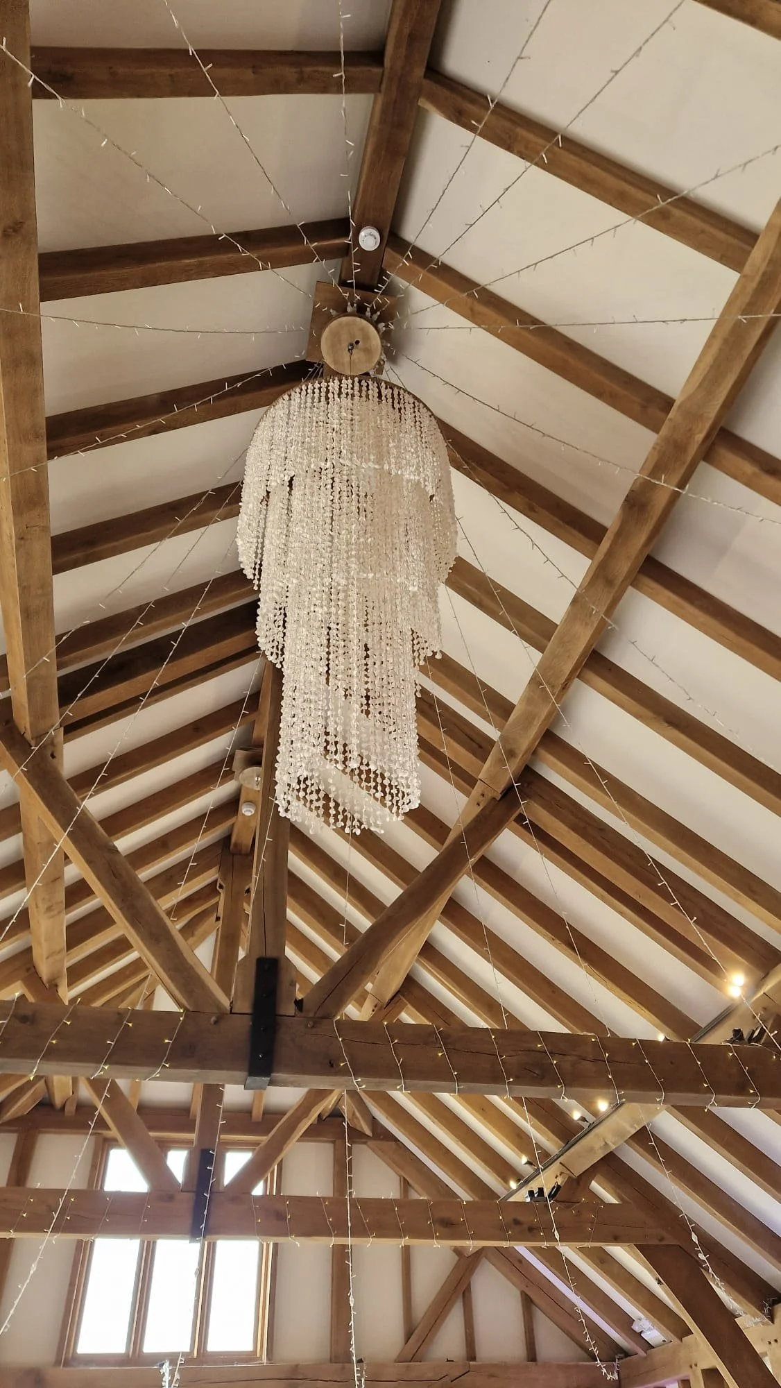 Shell Chandelier - Large hanging from wooden beams in a bright venue, available to hire for your wedding or event.