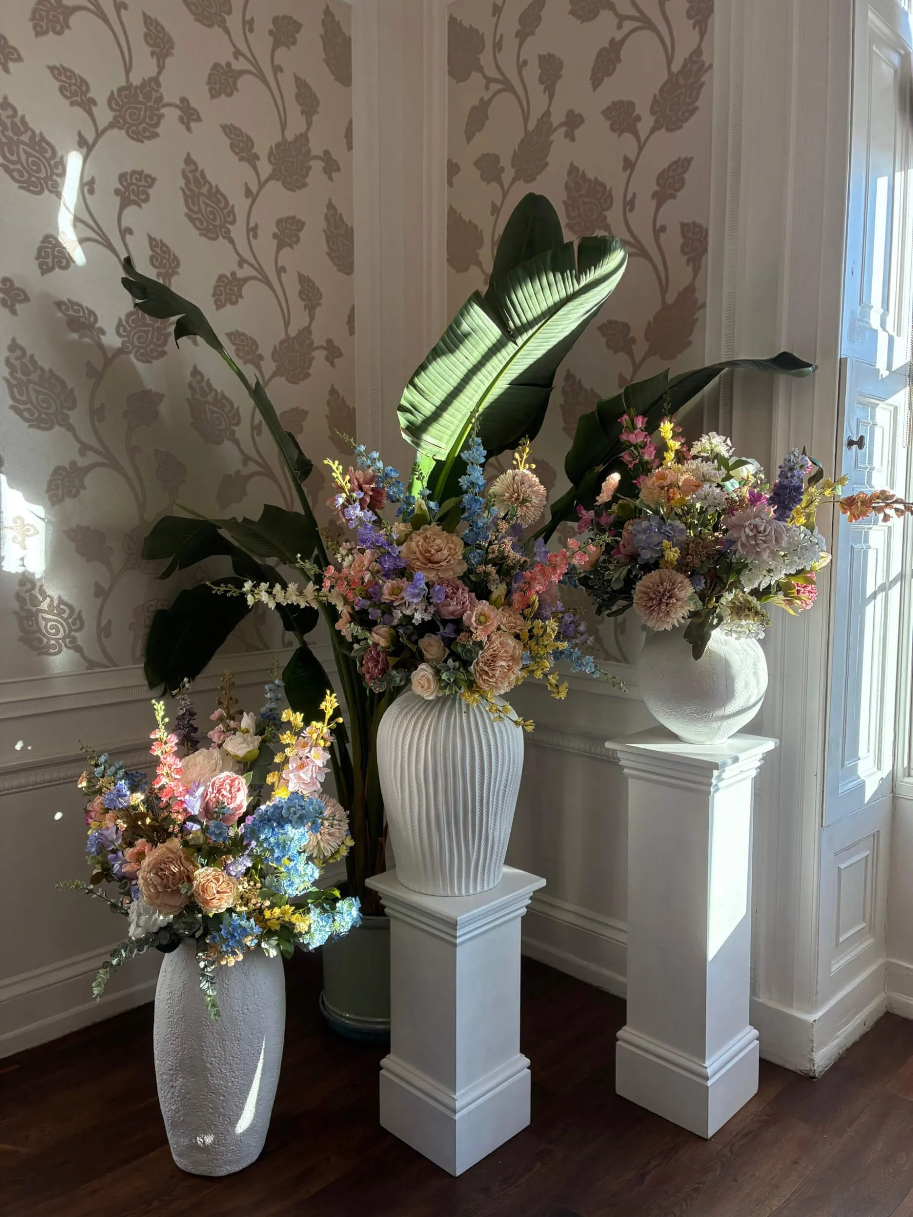 Ceramic White Clay Vase - Medium - 46cmH x 34.5cmW filled with pastel faux flowers on a white pedestal, available to hire for your wedding or event.