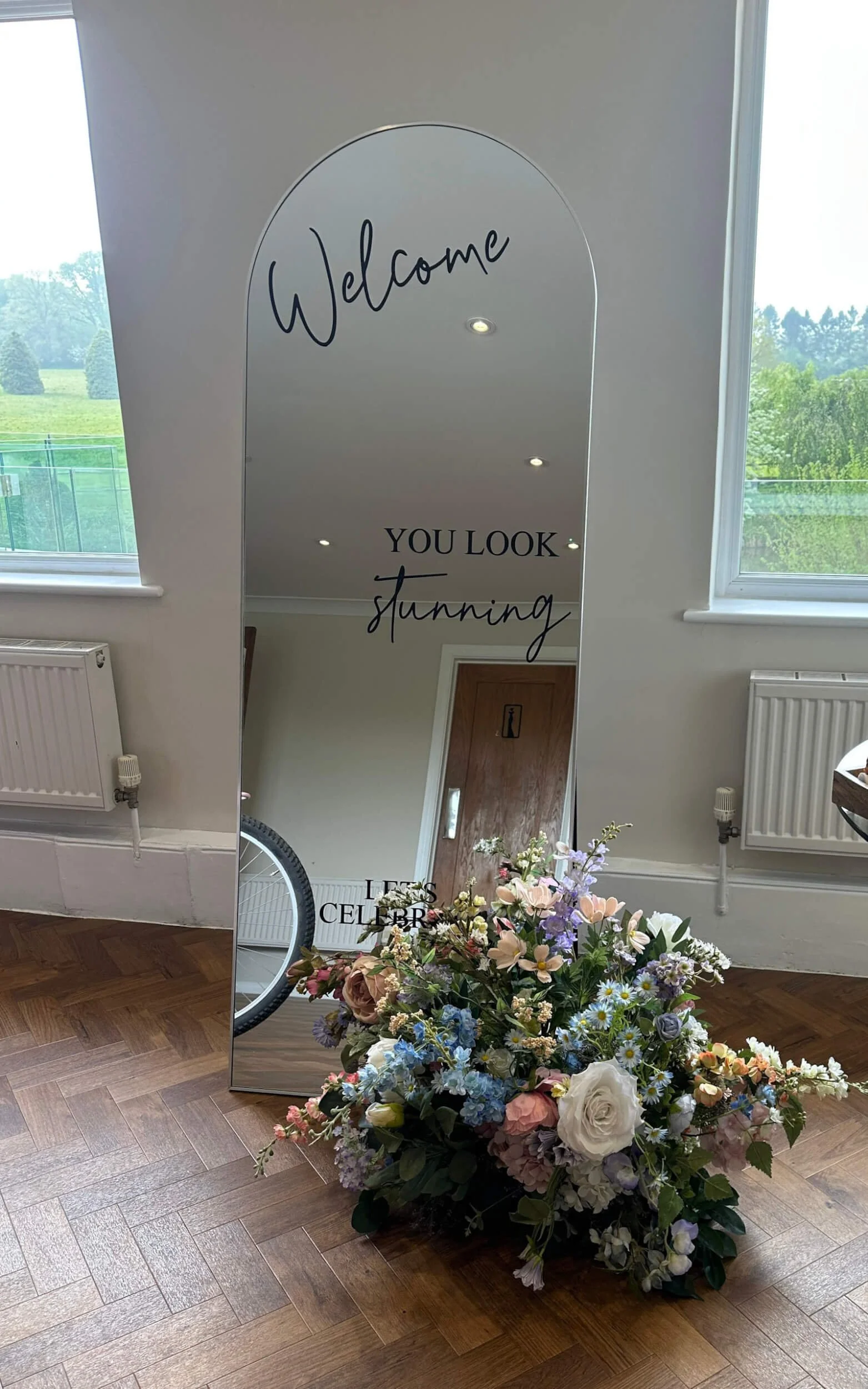Freestanding Arch Mirror - Silver - 176cm x 66cm with floral arrangement at base, available to hire for your wedding or event.