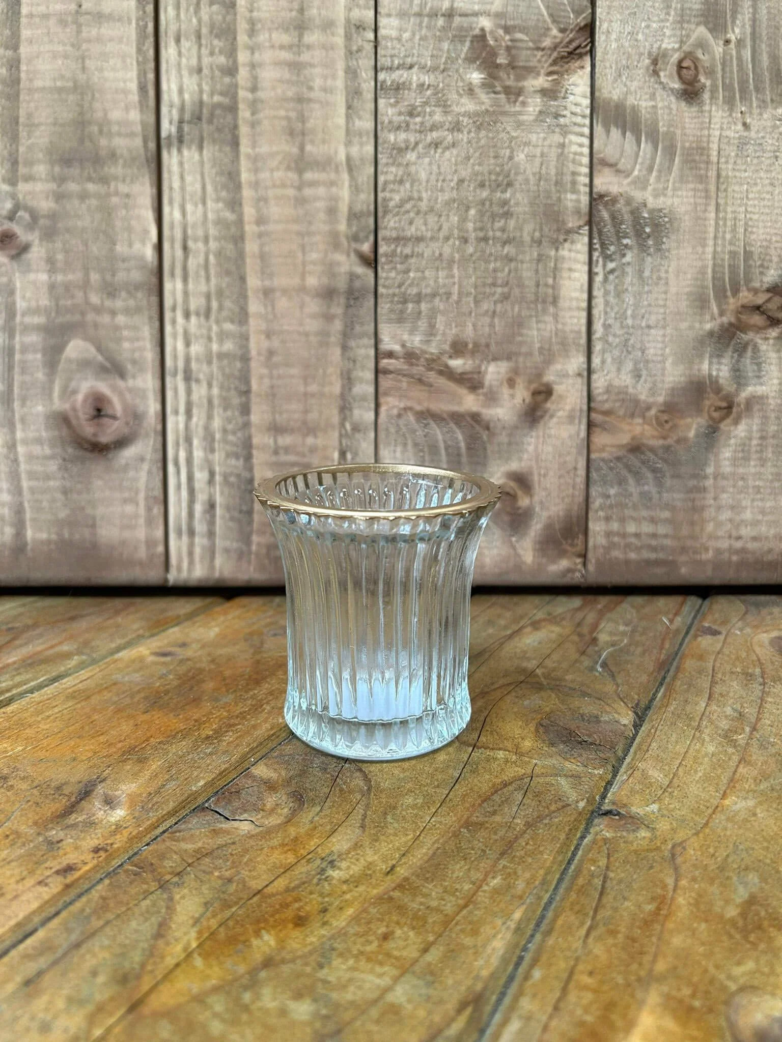 Fluted clear gold rim tealight holder on wooden surface with rustic wooden background, available to hire for your wedding or event.