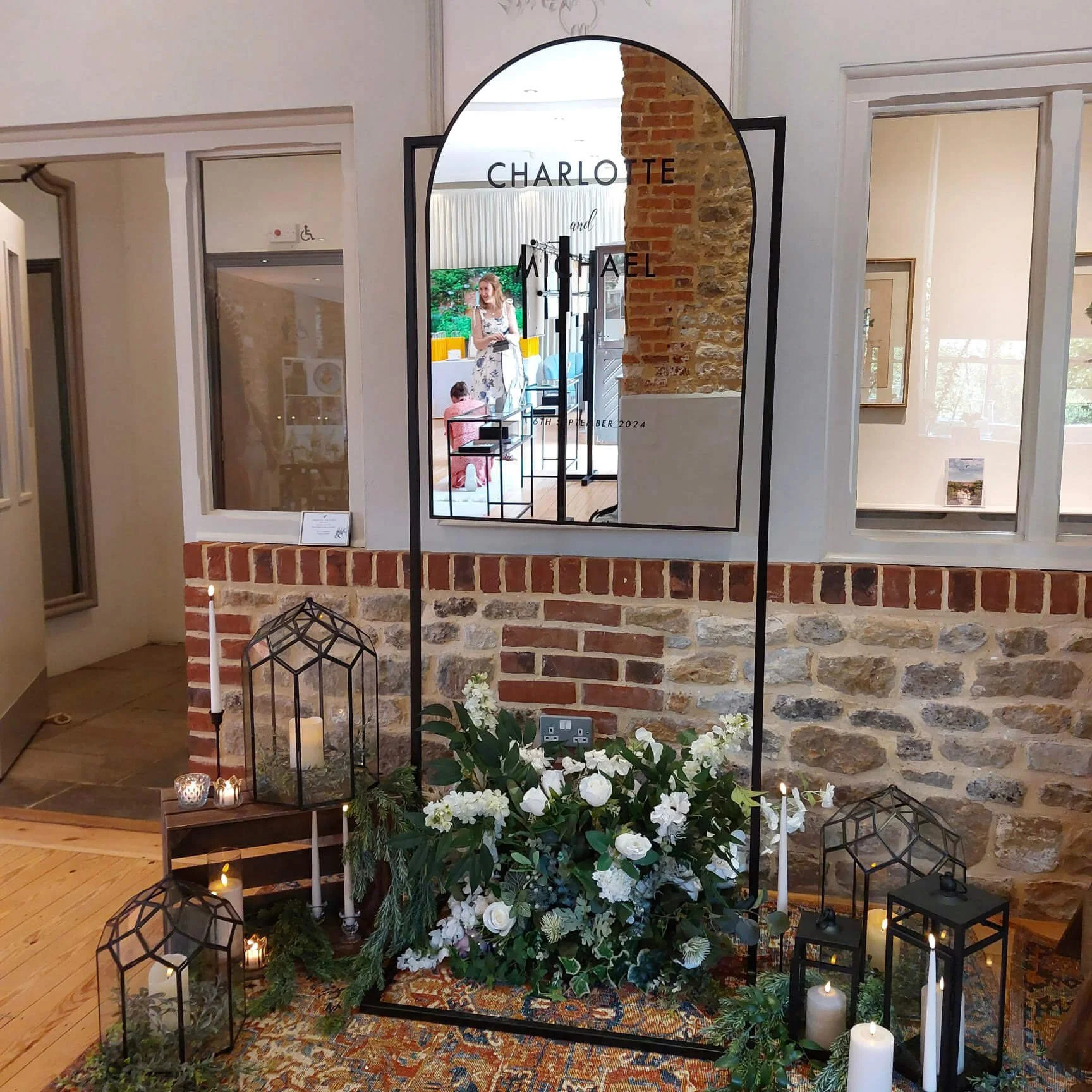Freestanding Arch Mirror - Black - 180cm x 76cm with curved top, surrounded by floral and candle decor, available to hire for your wedding or event.