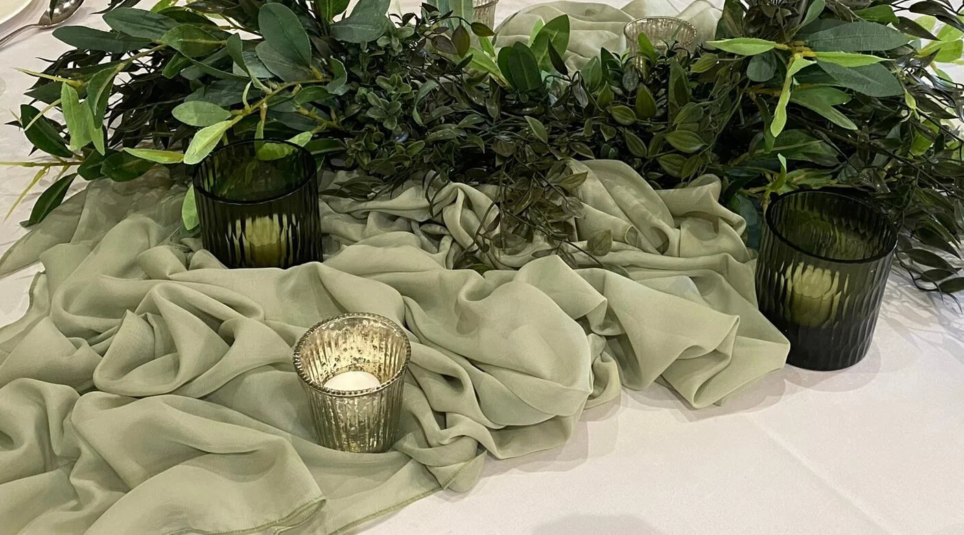 Green Fluted Tealight with lit candle, placed on green fabric and surrounded by greenery, available to hire for your wedding or event.