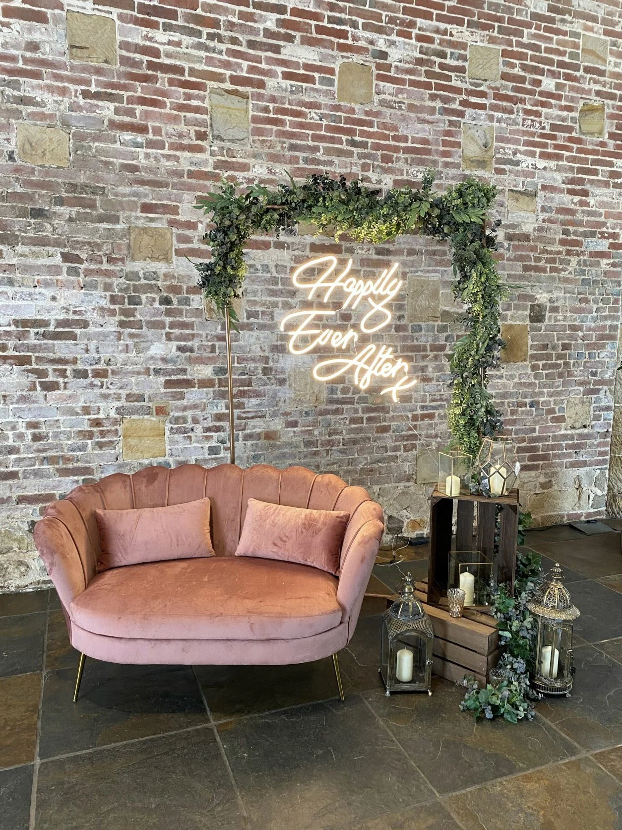 Luxe Velvet Pink Furniture - Love Seat/Sofa in pink velvet with cushions, styled with greenery arch and neon sign, available to hire for your wedding or event.