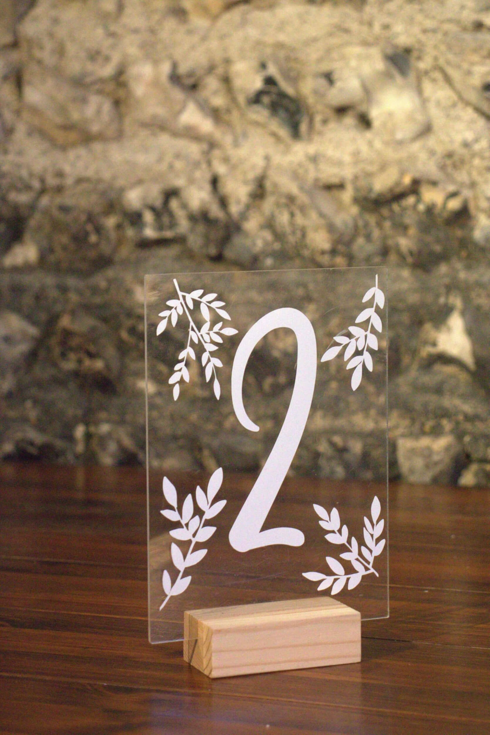 Perspex & Wood Table Numbers 1-12 featuring number 2 with white leaf designs on clear perspex, mounted on a wood block, available to hire for your wedding or event.