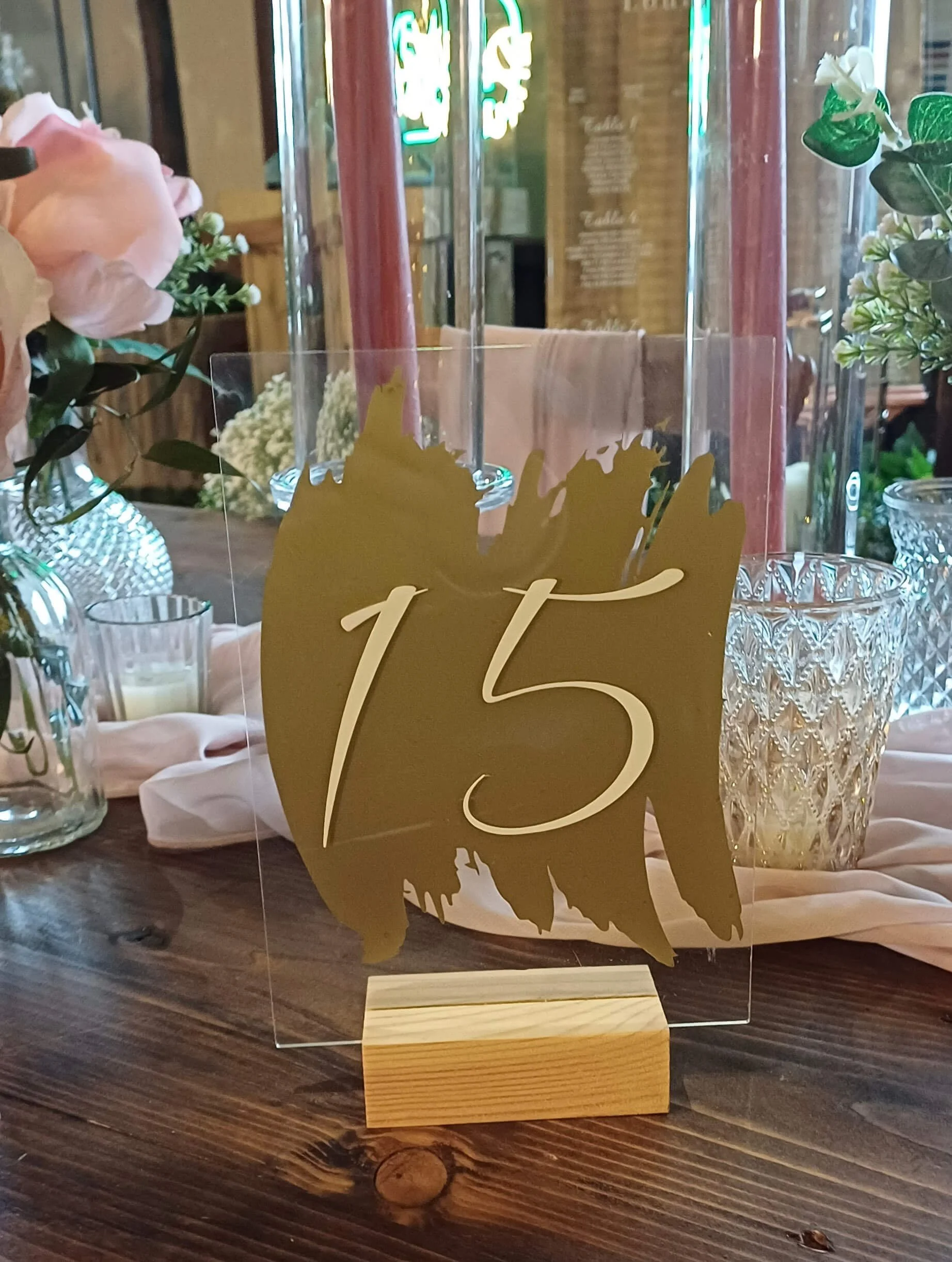 Gold Paint Effect Perspex and Wood Table Number 15 displayed on a wooden base, available to hire for your wedding or event with elegant pink candles and floral decor.