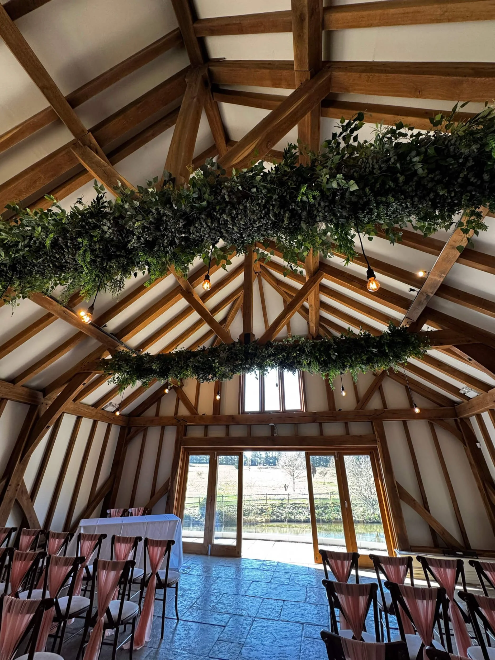 Faux Foliage Ceiling Decoration Bespoke Prices From featuring two long green garlands hanging from wooden beams, available to hire for your wedding or event.