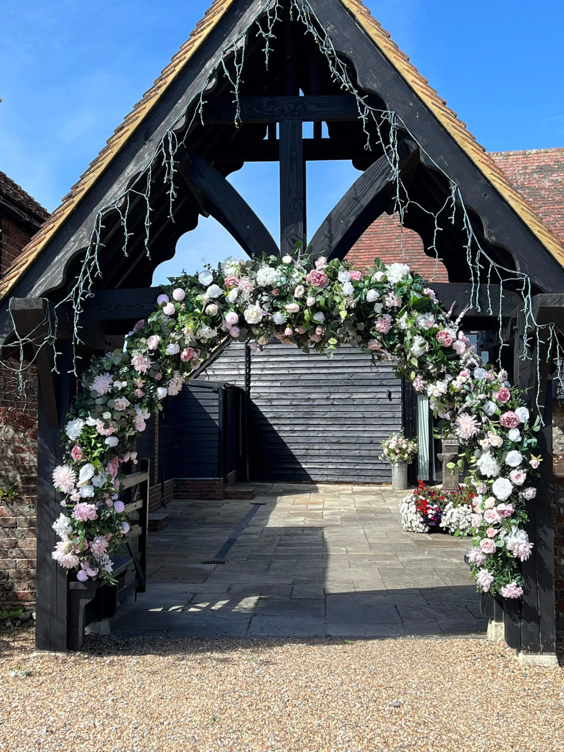 Faux Florals - Bespoke walk through arch decorated with pink, white, and green faux flowers, available to hire for your wedding or event.