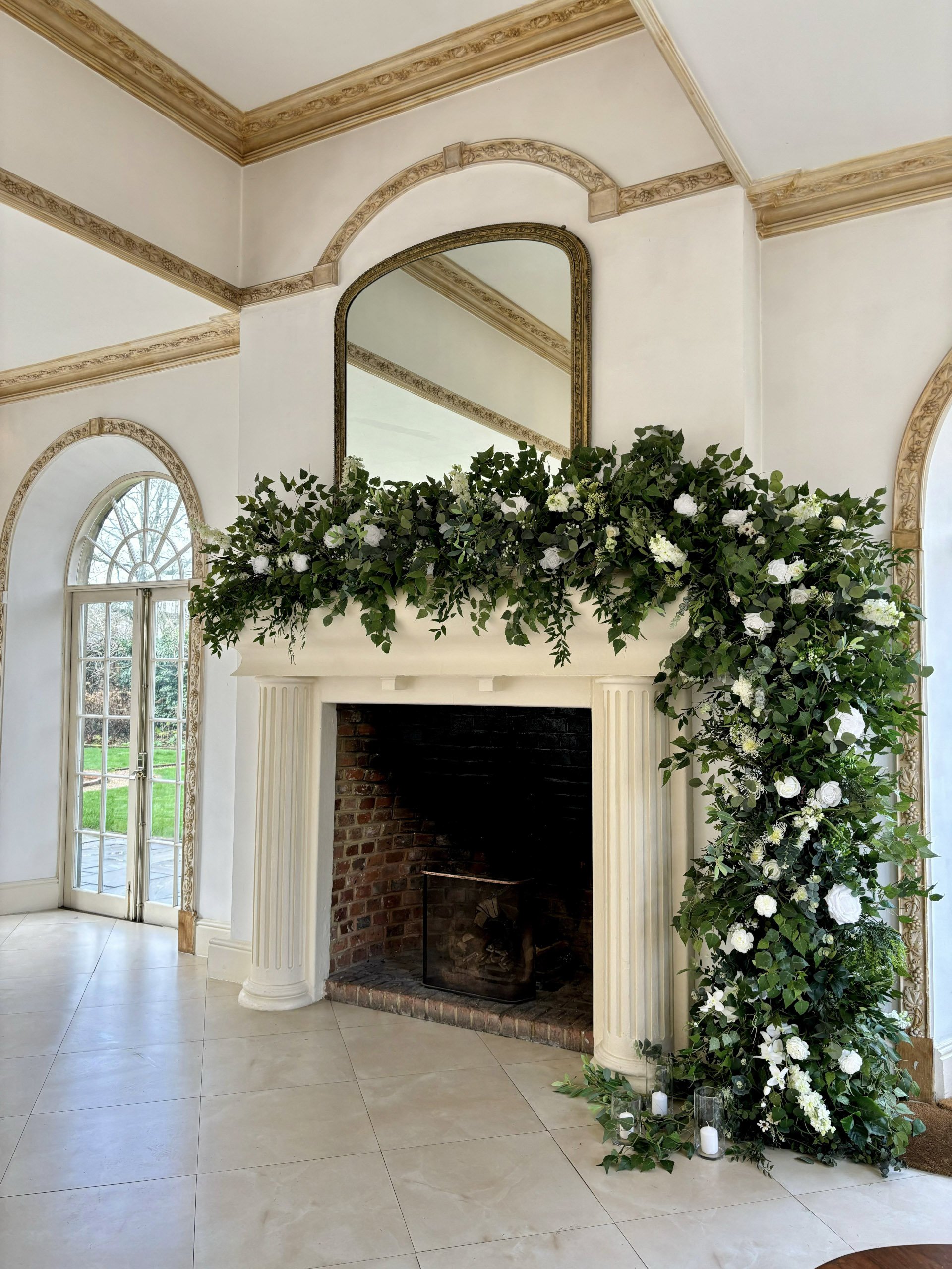 Faux Flower Accent Decor - Structures/Fireplaces/Staircases and more... Prices To with lush green foliage and white flowers on a cream fireplace, available to hire for your wedding or event.