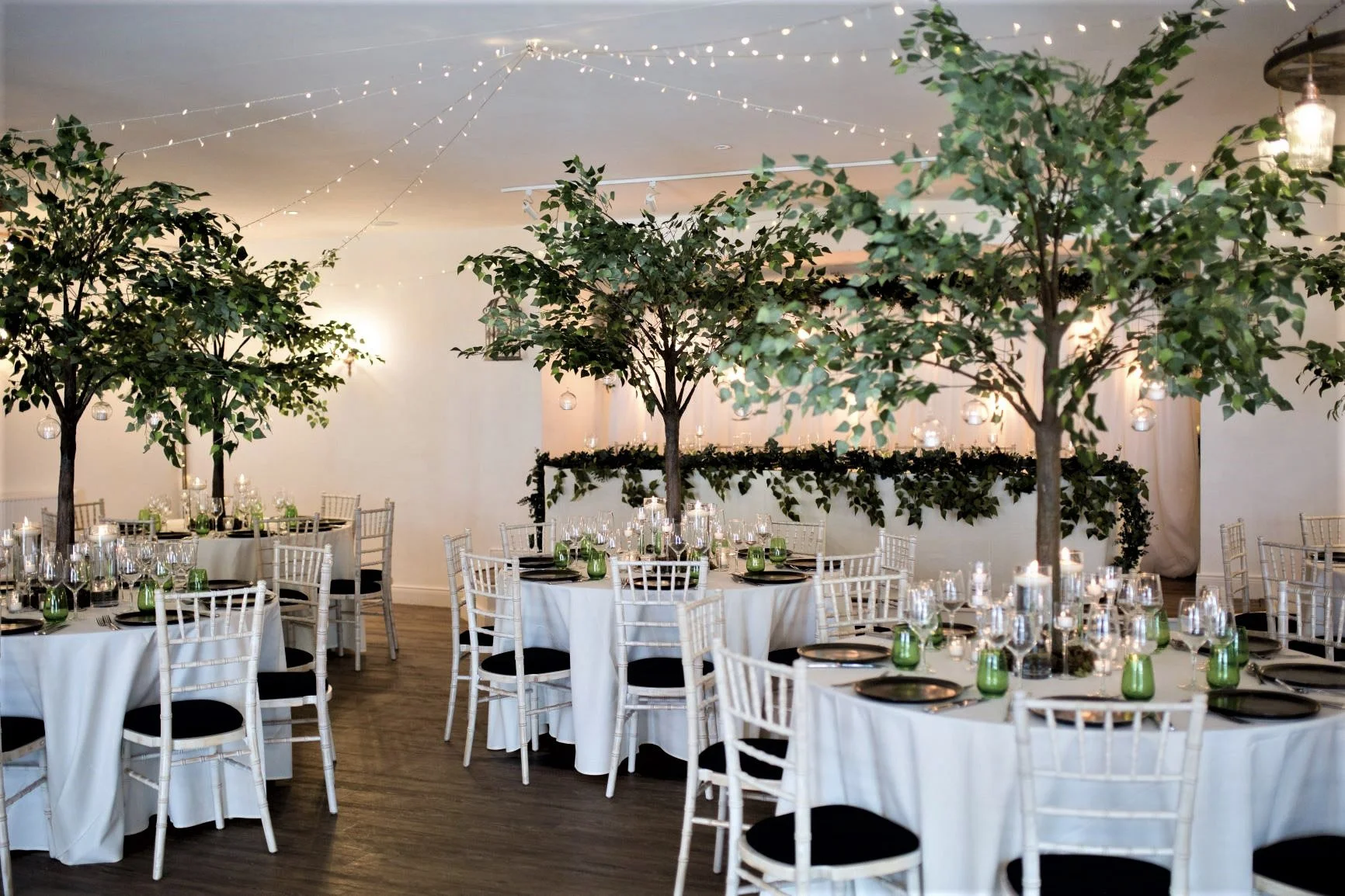 Faux Foliage decoration for tables Prices To styled as Faux Foliage decoration for tables featuring tall green faux trees as centrepieces, available to hire for your wedding or event.