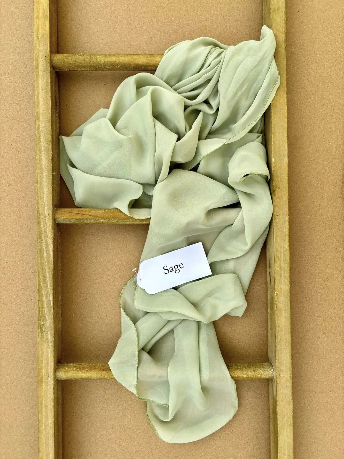 Chiffon Table Runner - Sage Green draped on a wooden ladder, available to hire for your wedding or event.